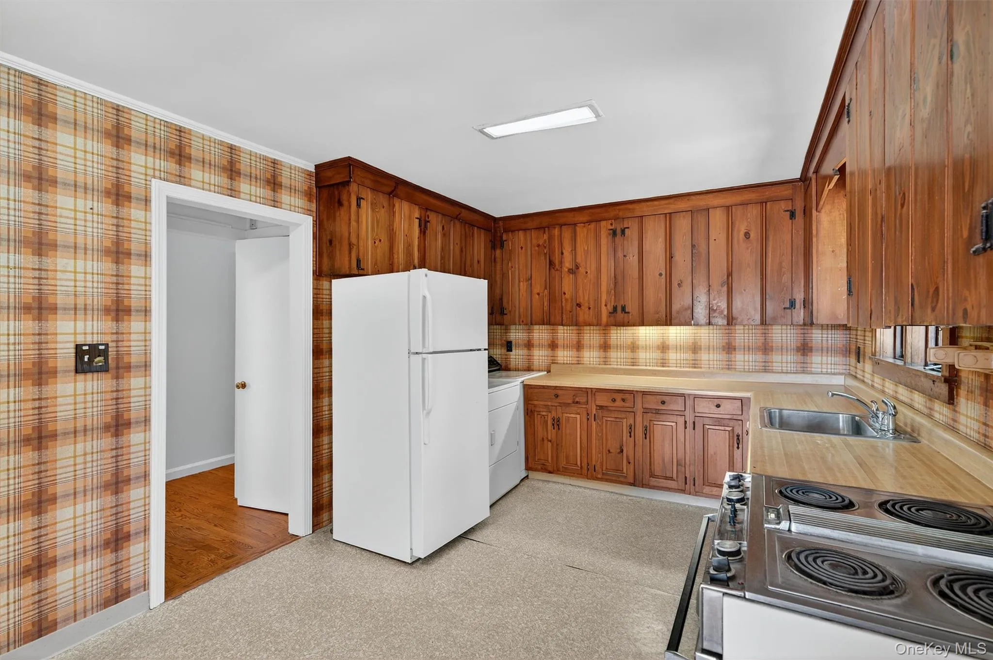 Kitchen with freestanding refrigerator, light countertops, electric range, brown cabinets, and washer / clothes dryer Kitchen with freestanding refrigerator, light countertops, electric range, brown cabinets, and washer / clothes dryer