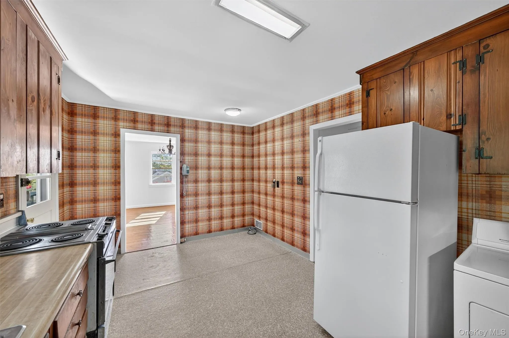 Kitchen with washer / dryer, freestanding refrigerator, stainless steel range with electric stovetop, wallpapered walls, and light countertops Kitchen with washer / dryer, freestanding refrigerator, stainless steel range with electric stovetop, wallpapered walls, and light countertops
