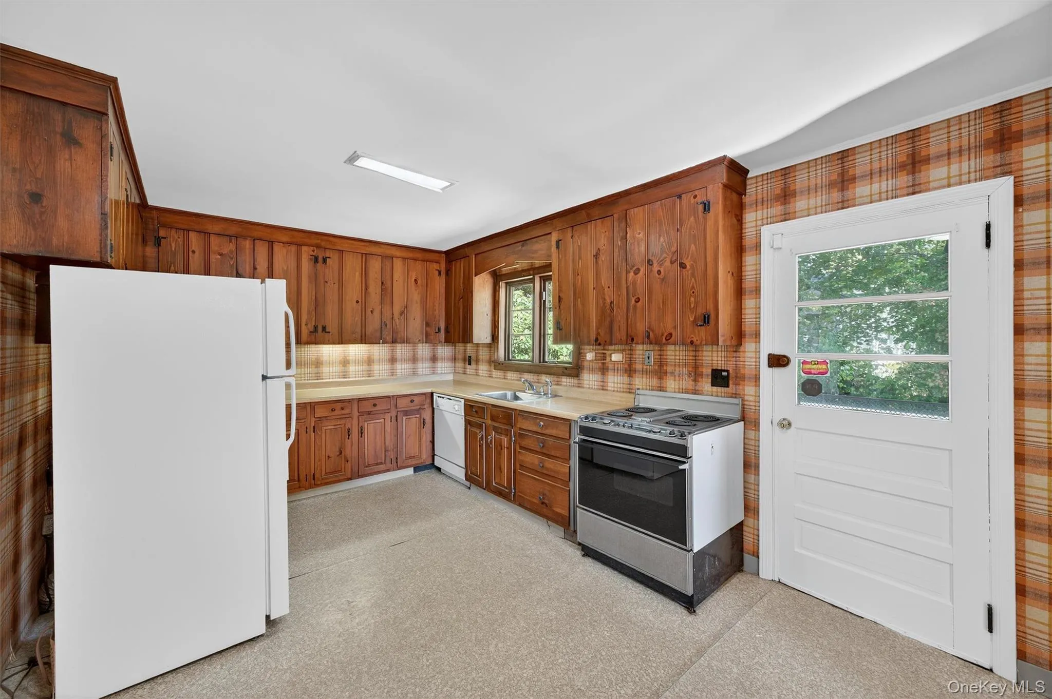 Kitchen with white appliances, light countertops, brown cabinets, light floors, and wood walls Kitchen with white appliances, light countertops, brown cabinets, light floors, and wood walls