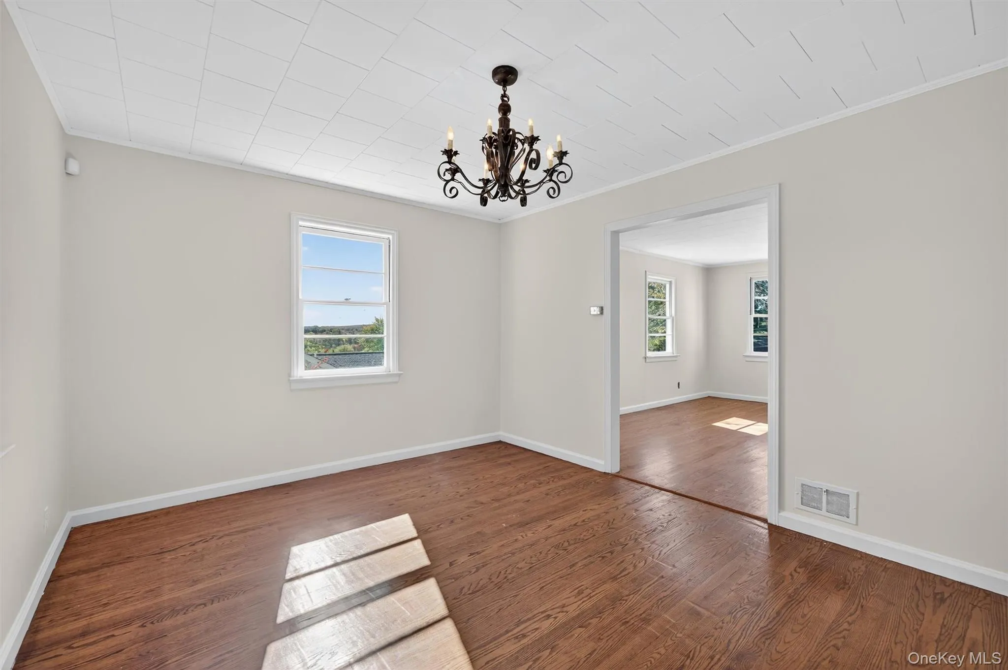 Unfurnished room with a chandelier, dark wood-style floors, crown molding, and plenty of natural light Unfurnished room with a chandelier, dark wood-style floors, crown molding, and plenty of natural light