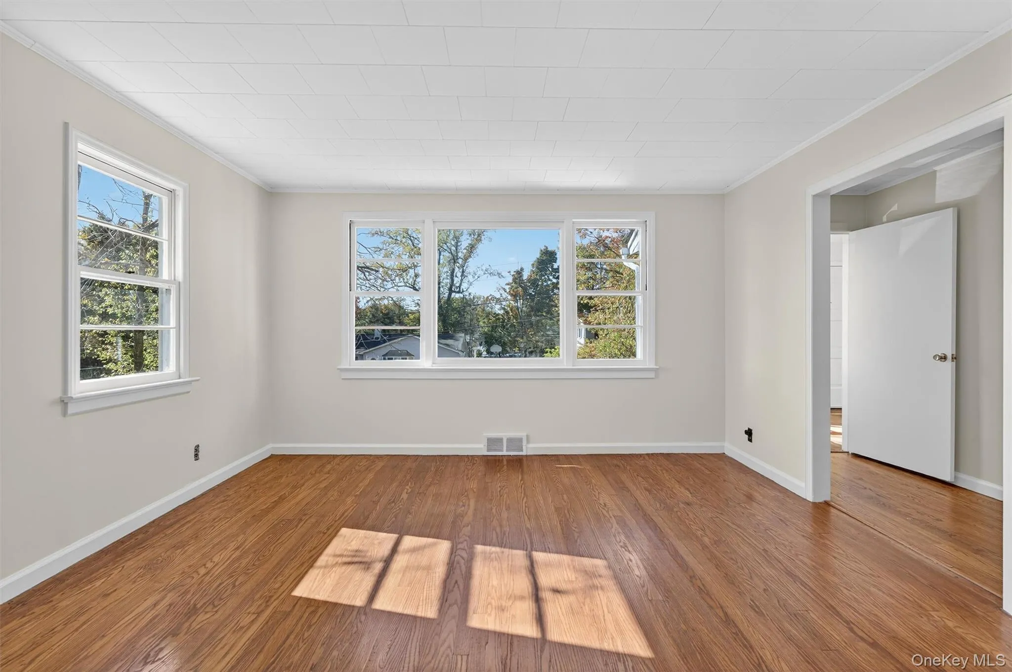 Empty room with ornamental molding, wood finished floors, and plenty of natural light Empty room with ornamental molding, wood finished floors, and plenty of natural light