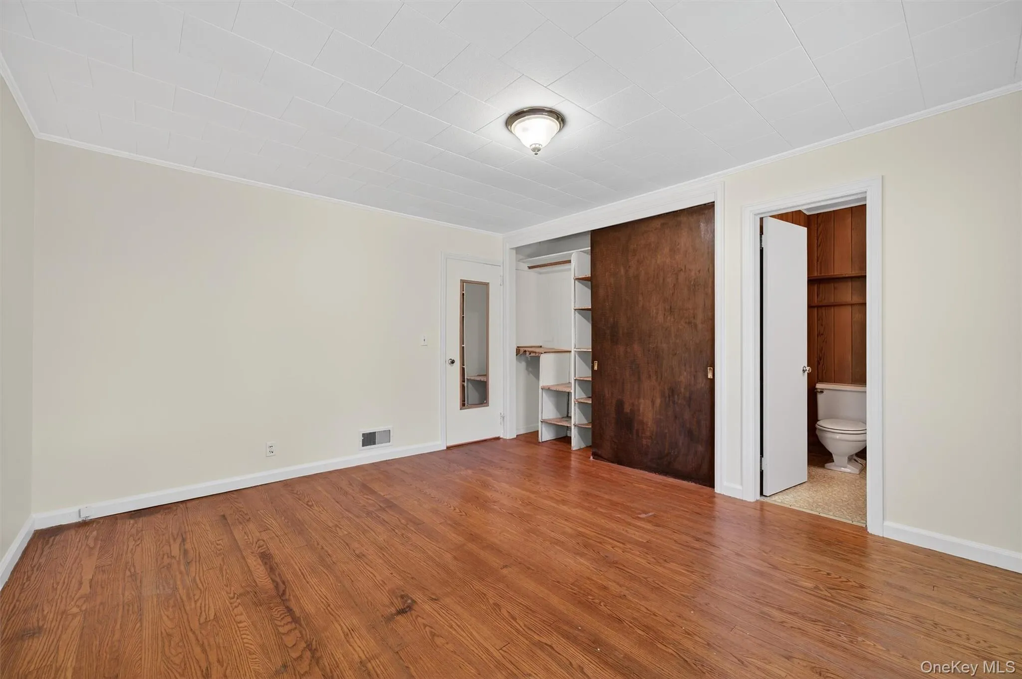 Unfurnished bedroom featuring crown molding, a closet, wood finished floors, and ensuite bathroom Unfurnished bedroom featuring crown molding, a closet, wood finished floors, and ensuite bathroom