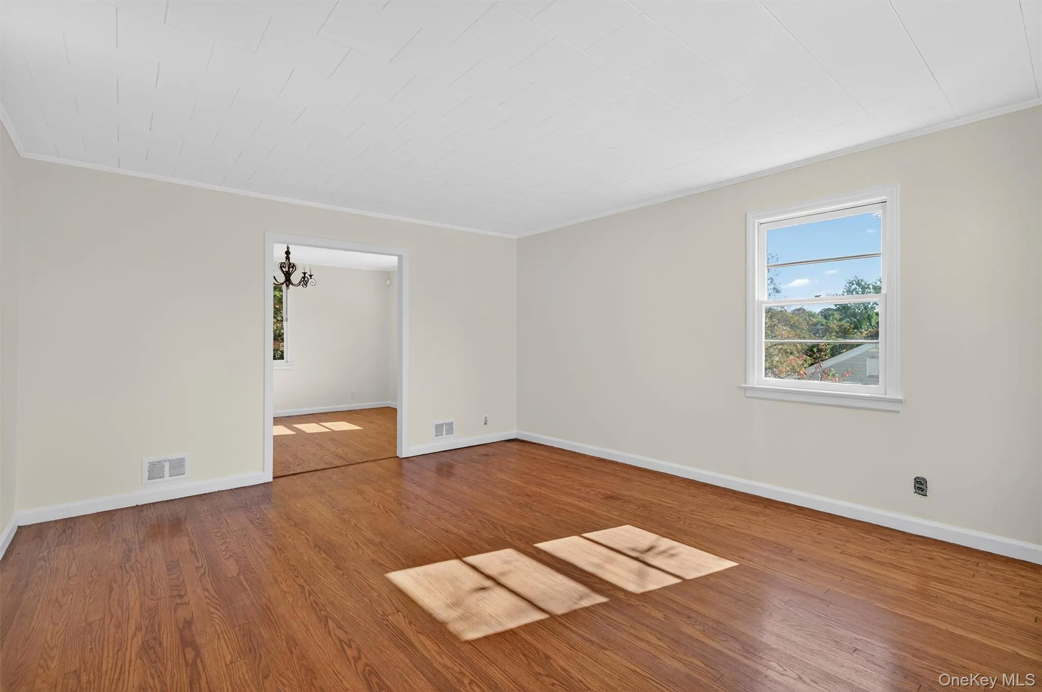 Empty room featuring ornamental molding, wood finished floors, and a chandelier Empty room featuring ornamental molding, wood finished floors, and a chandelier