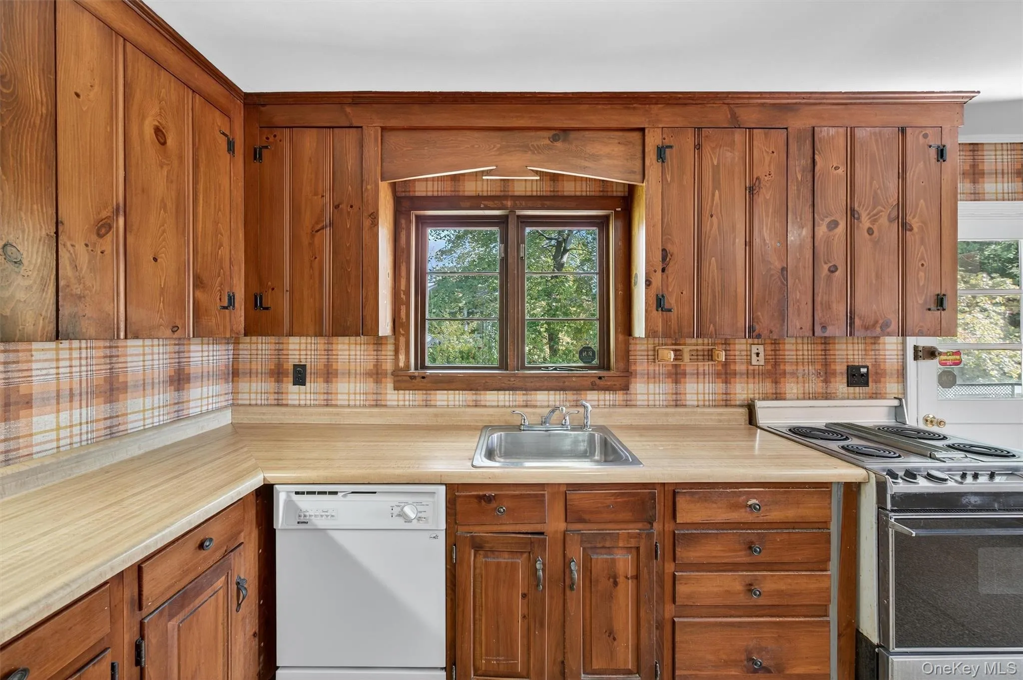 Kitchen featuring range with electric cooktop, white dishwasher, light countertops, brown cabinets, and backsplash Kitchen featuring range with electric cooktop, white dishwasher, light countertops, brown cabinets, and backsplash