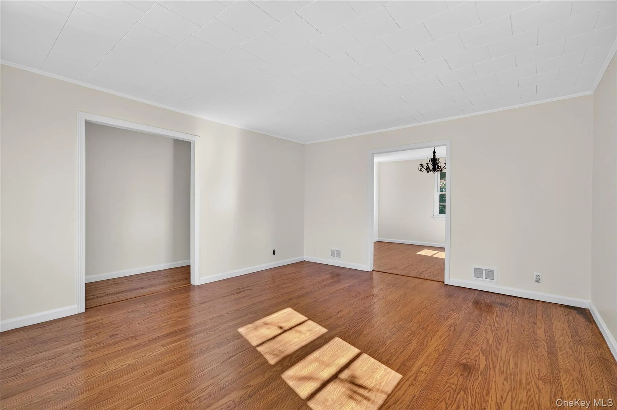 Empty room with ornamental molding, a chandelier, and wood finished floors Empty room with ornamental molding, a chandelier, and wood finished floors