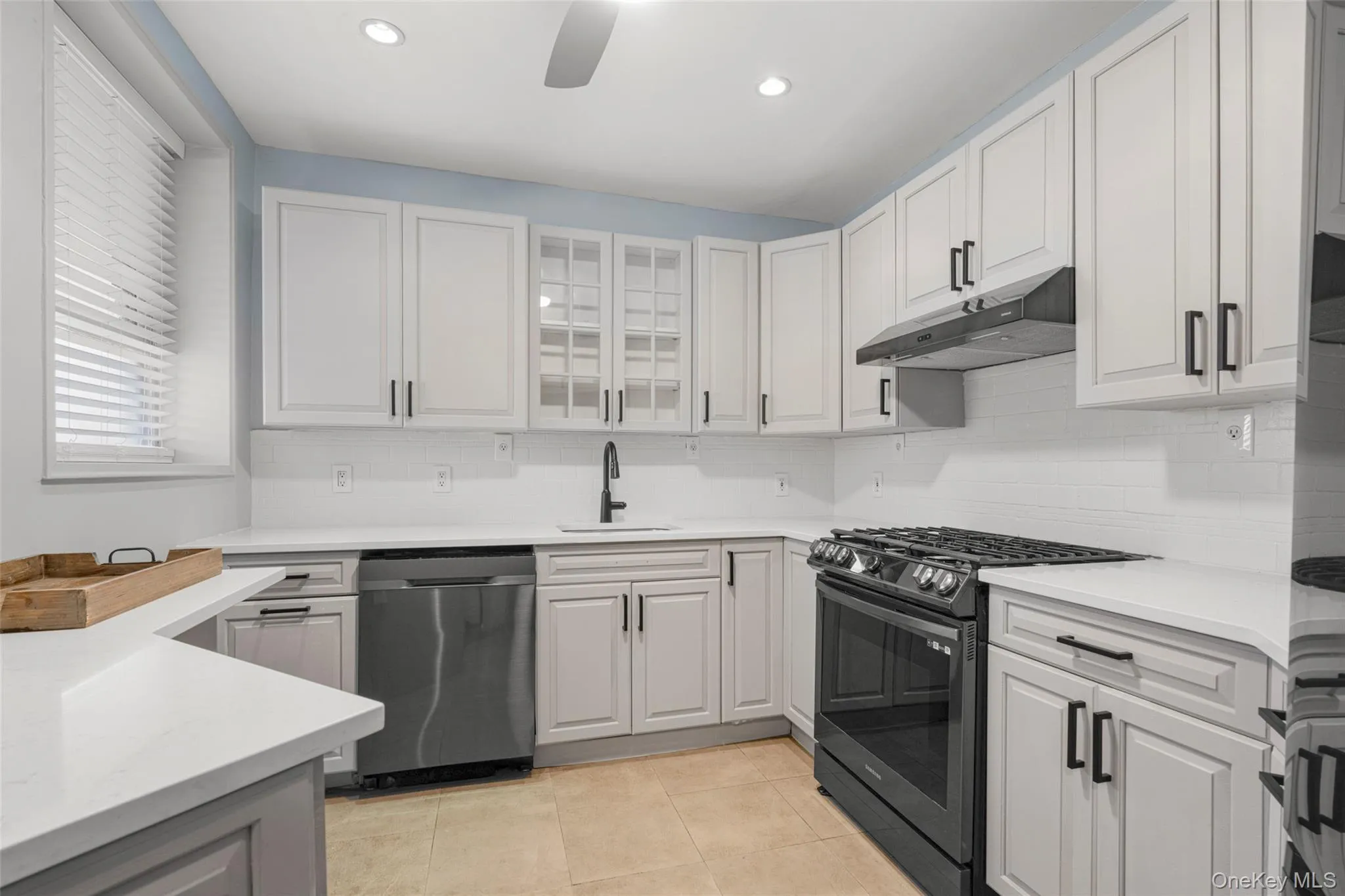 Kitchen with stainless steel appliances, glass insert cabinets, tasteful backsplash, under cabinet range hood, and light tile patterned flooring Kitchen with stainless steel appliances, glass insert cabinets, tasteful backsplash, under cabinet range hood, and light tile patterned flooring