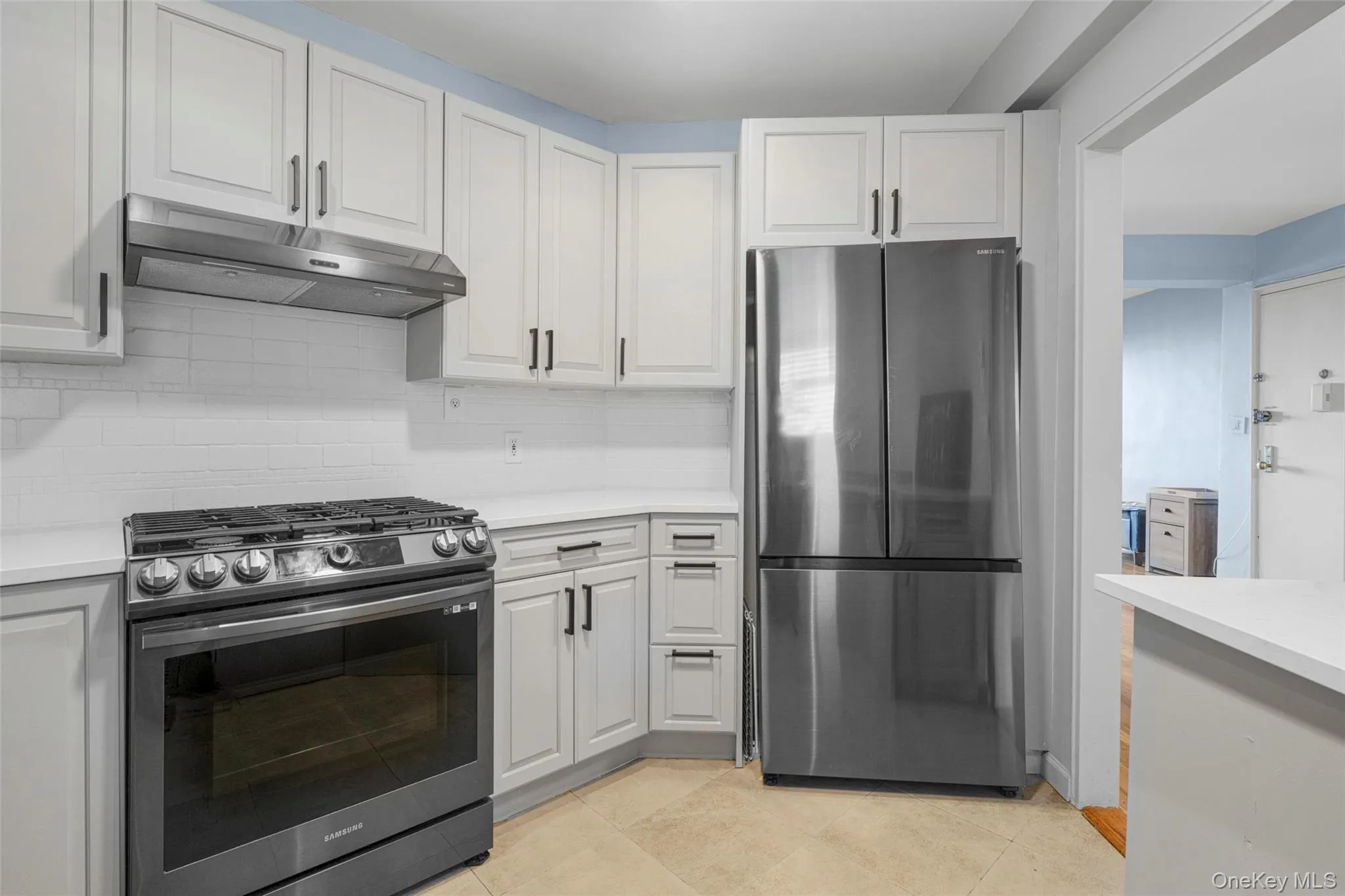 Kitchen with stainless steel appliances, under cabinet range hood, light tile patterned floors, decorative backsplash, and white cabinets Kitchen with stainless steel appliances, under cabinet range hood, light tile patterned floors, decorative backsplash, and white cabinets