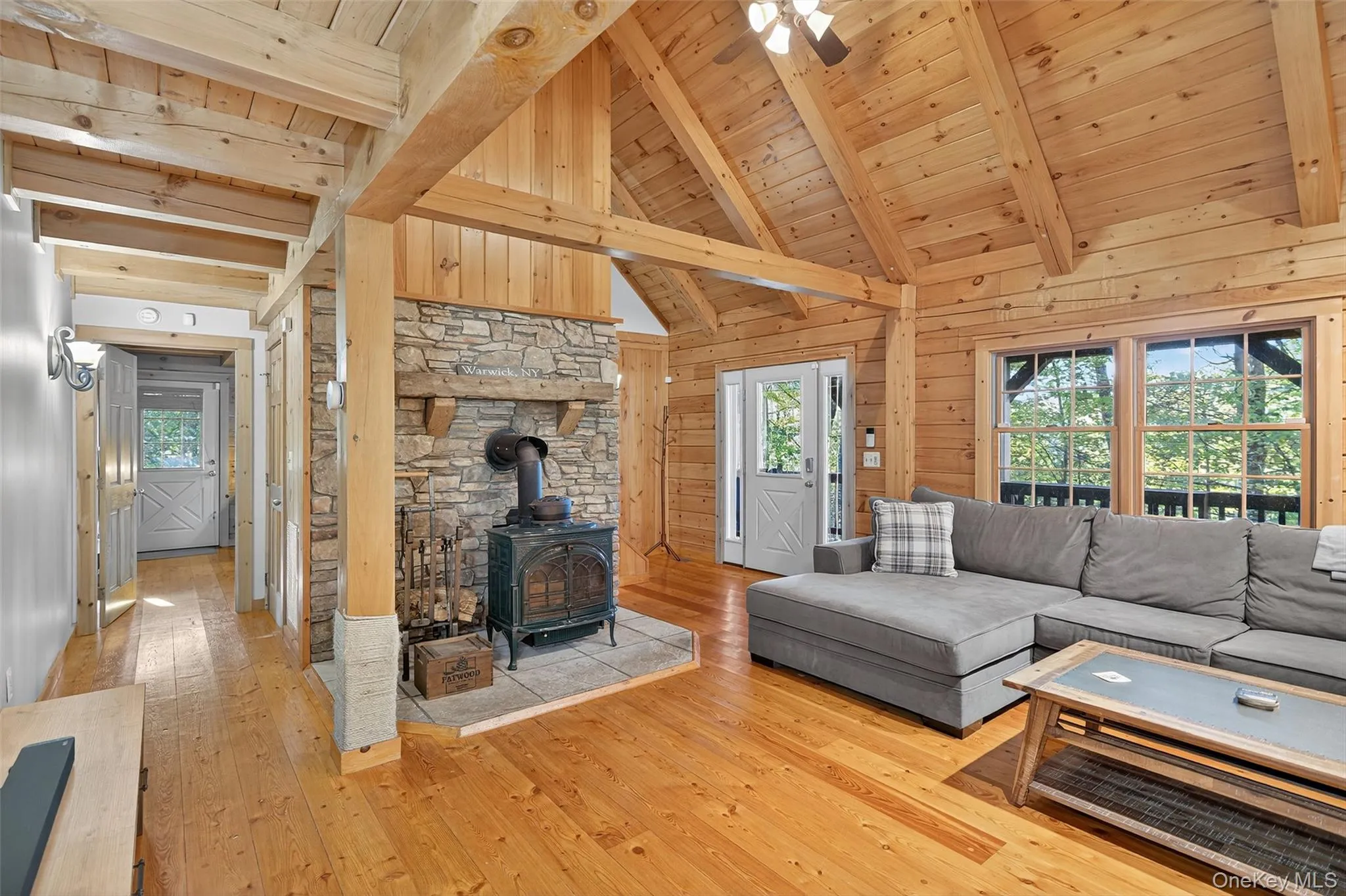 Living area featuring a wood stove, light wood-style flooring, a wooden ceiling with exposed beams, high vaulted ceiling, and wooden walls Living area featuring a wood stove, light wood-style flooring, a wooden ceiling with exposed beams, high vaulted ceiling, and wooden walls