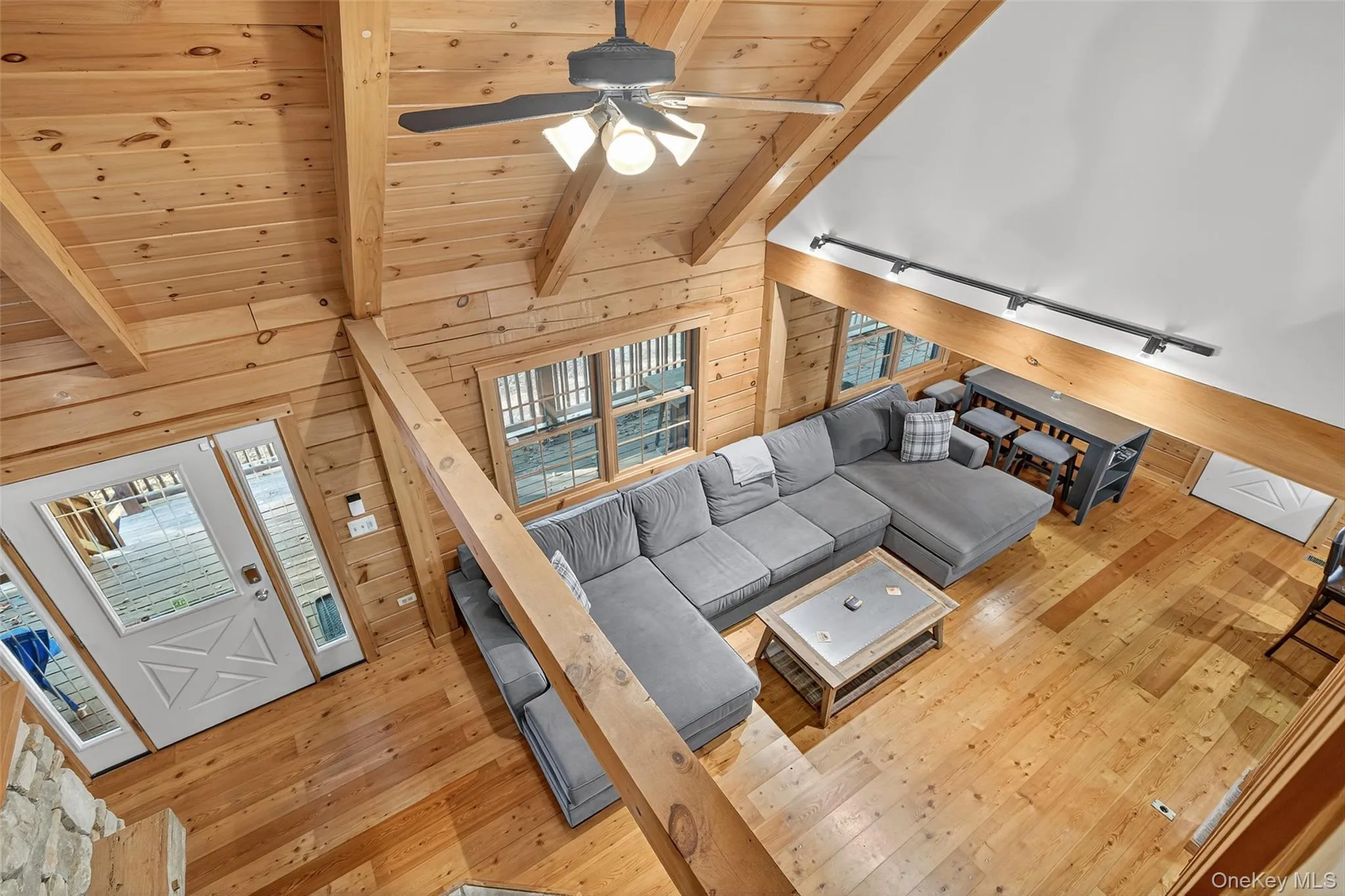 Living room featuring wooden walls, light wood finished floors, a ceiling fan, high vaulted ceiling, and a wooden ceiling with exposed beams Living room featuring wooden walls, light wood finished floors, a ceiling fan, high vaulted ceiling, and a wooden ceiling with exposed beams