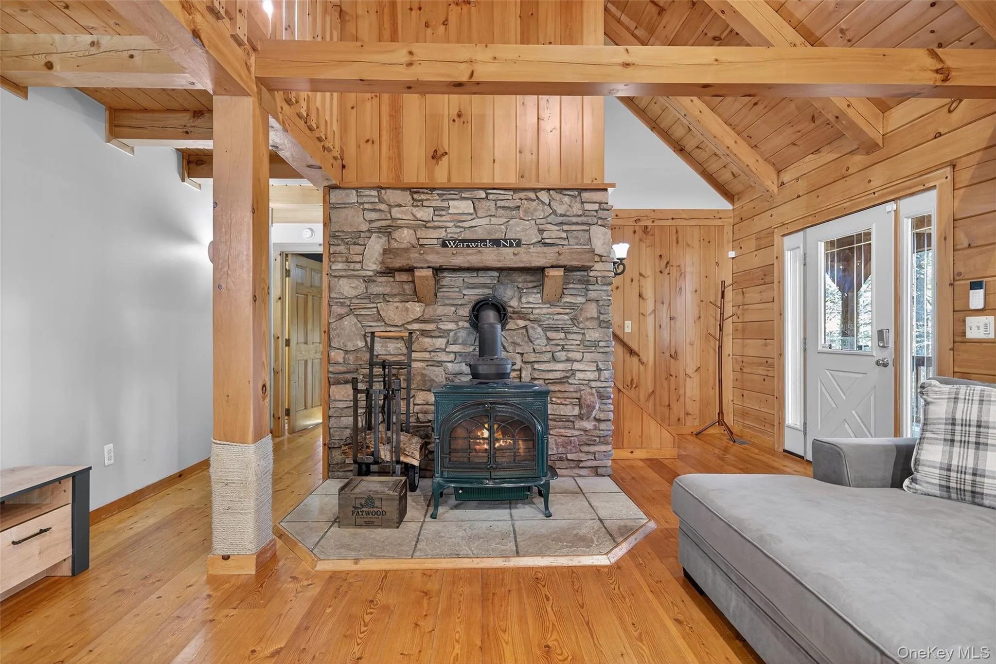 Living area with a wood stove, hardwood / wood-style floors, a wood ceiling with exposed beams, wooden walls, and high vaulted ceiling Living area with a wood stove, hardwood / wood-style floors, a wood ceiling with exposed beams, wooden walls, and high vaulted ceiling