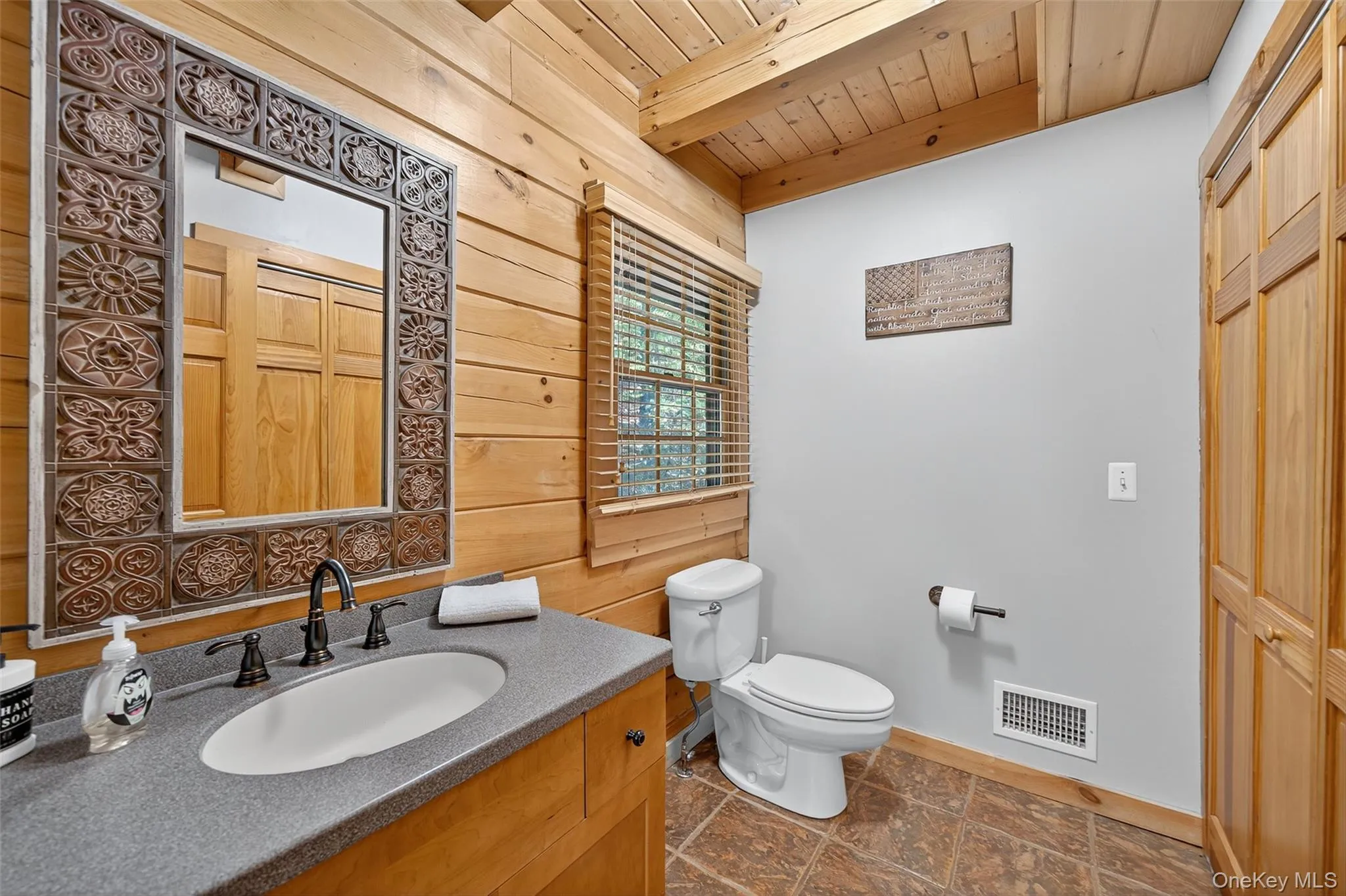 Bathroom featuring vanity, a wooden ceiling with exposed beams, wood walls, and dark stone finish floors Bathroom featuring vanity, a wooden ceiling with exposed beams, wood walls, and dark stone finish floors