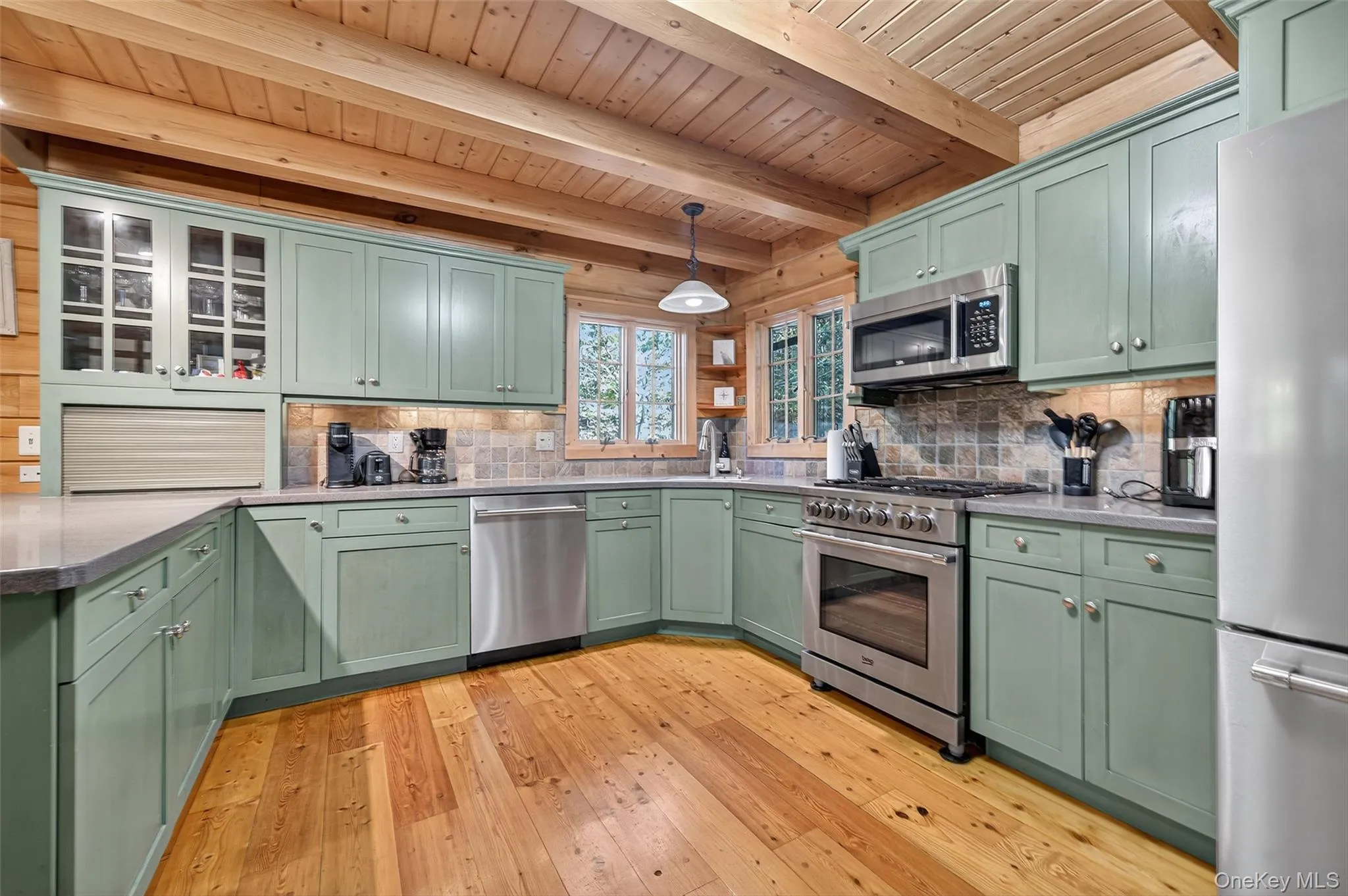 Kitchen with green cabinets, stainless steel appliances, light wood-style floors, hanging light fixtures, and a wooden ceiling with exposed beams Kitchen with green cabinets, stainless steel appliances, light wood-style floors, hanging light fixtures, and a wooden ceiling with exposed beams