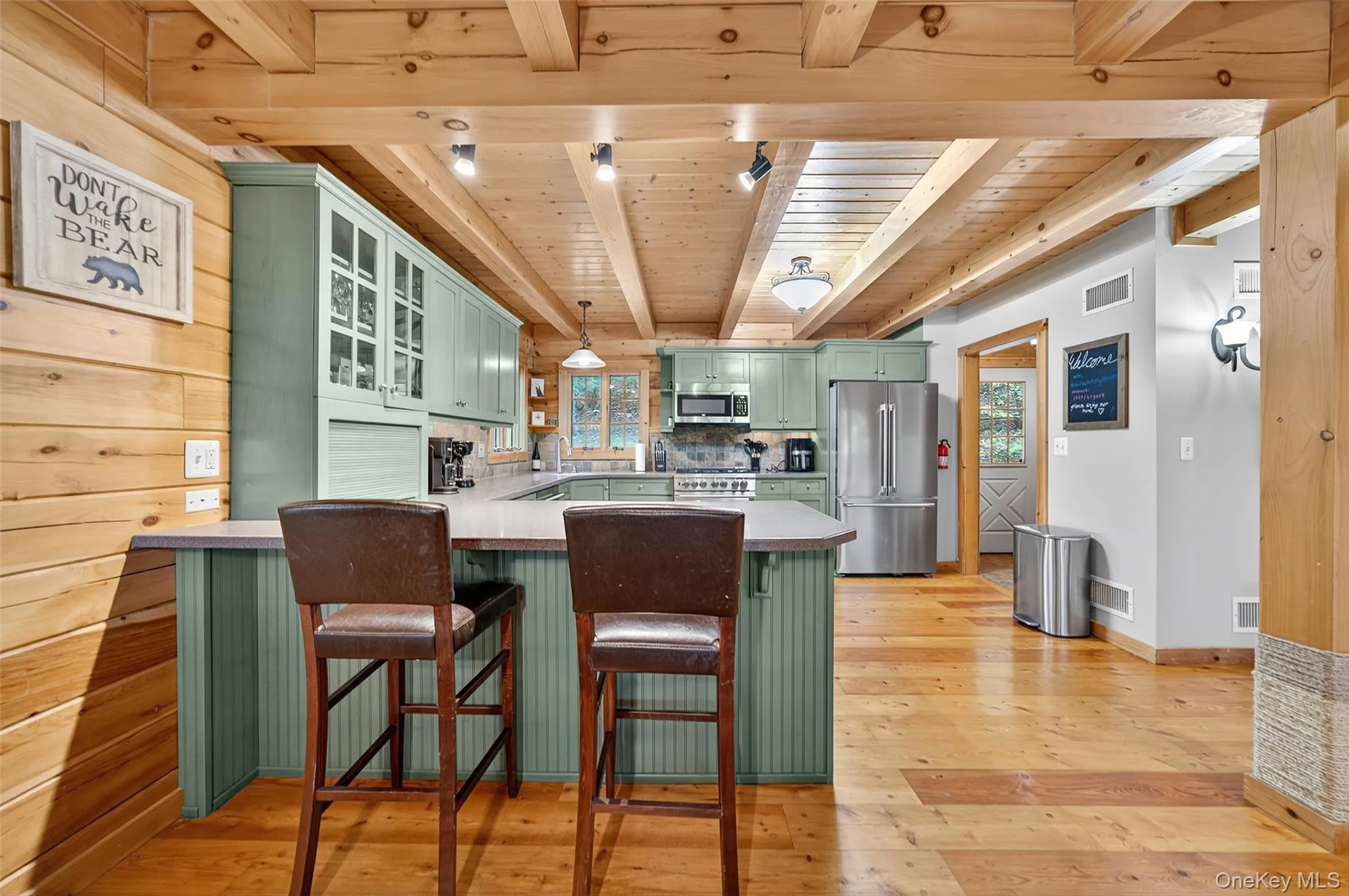 Kitchen with green cabinets, glass insert cabinets, light wood-style flooring, a kitchen bar, and a wood ceiling with exposed beams Kitchen with green cabinets, glass insert cabinets, light wood-style flooring, a kitchen bar, and a wood ceiling with exposed beams