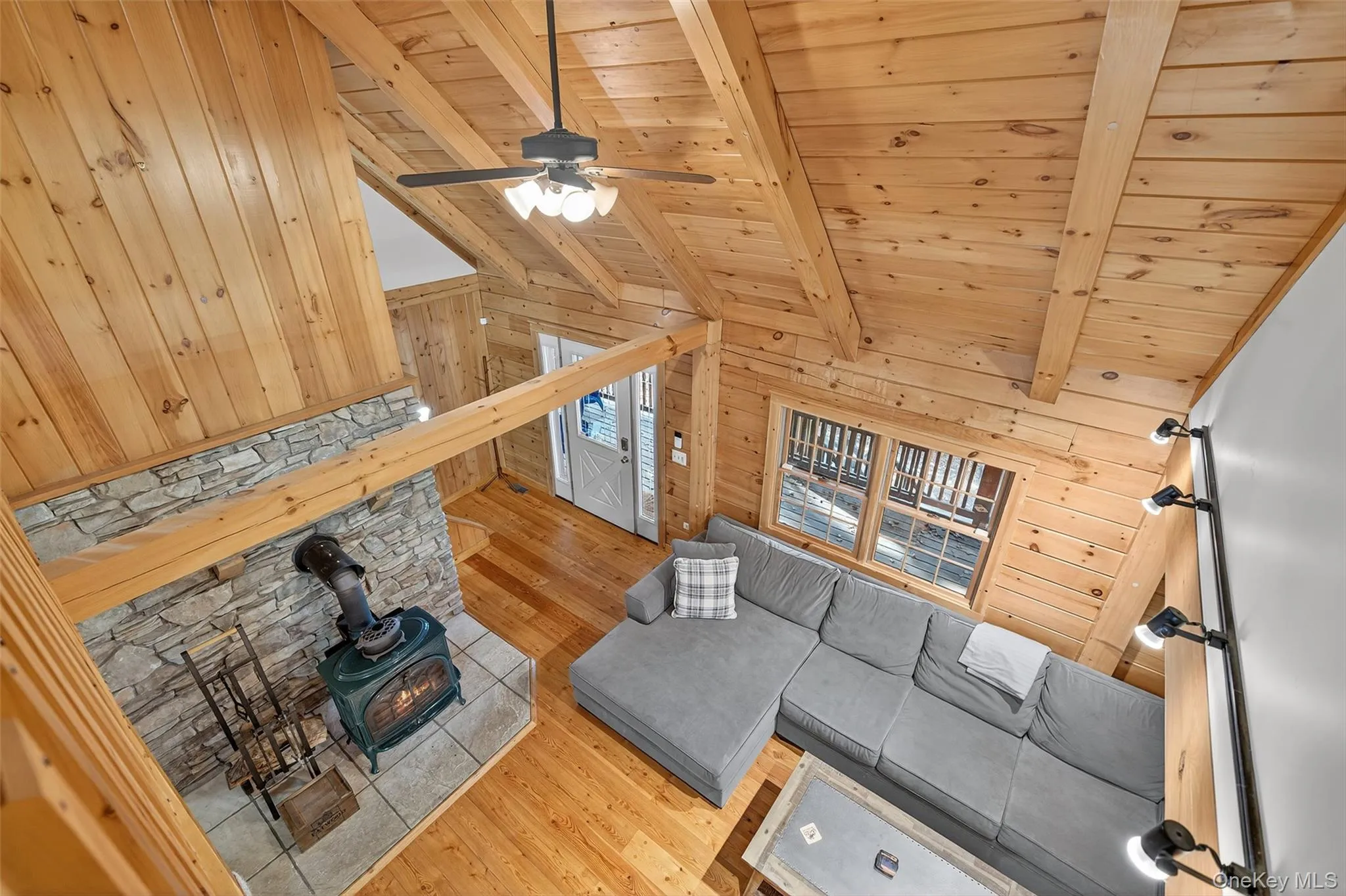 Living room with wood walls, light wood-style floors, high vaulted ceiling, a wood stove, and a wooden ceiling with exposed beams Living room with wood walls, light wood-style floors, high vaulted ceiling, a wood stove, and a wooden ceiling with exposed beams