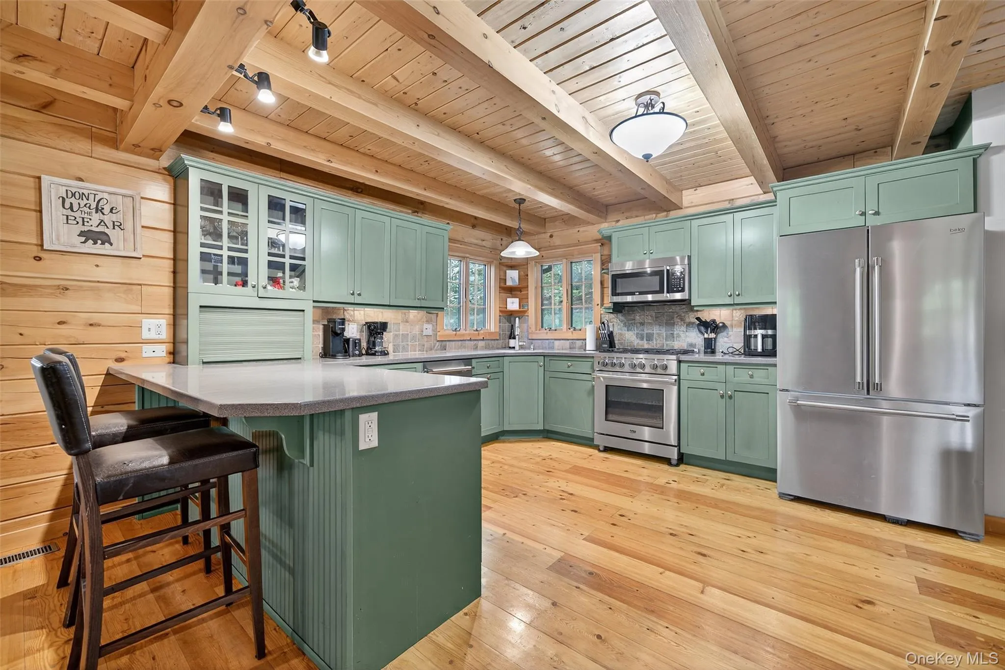 Kitchen with green cabinets, premium appliances, glass insert cabinets, a kitchen breakfast bar, and a wooden ceiling with exposed beams Kitchen with green cabinets, premium appliances, glass insert cabinets, a kitchen breakfast bar, and a wooden ceiling with exposed beams