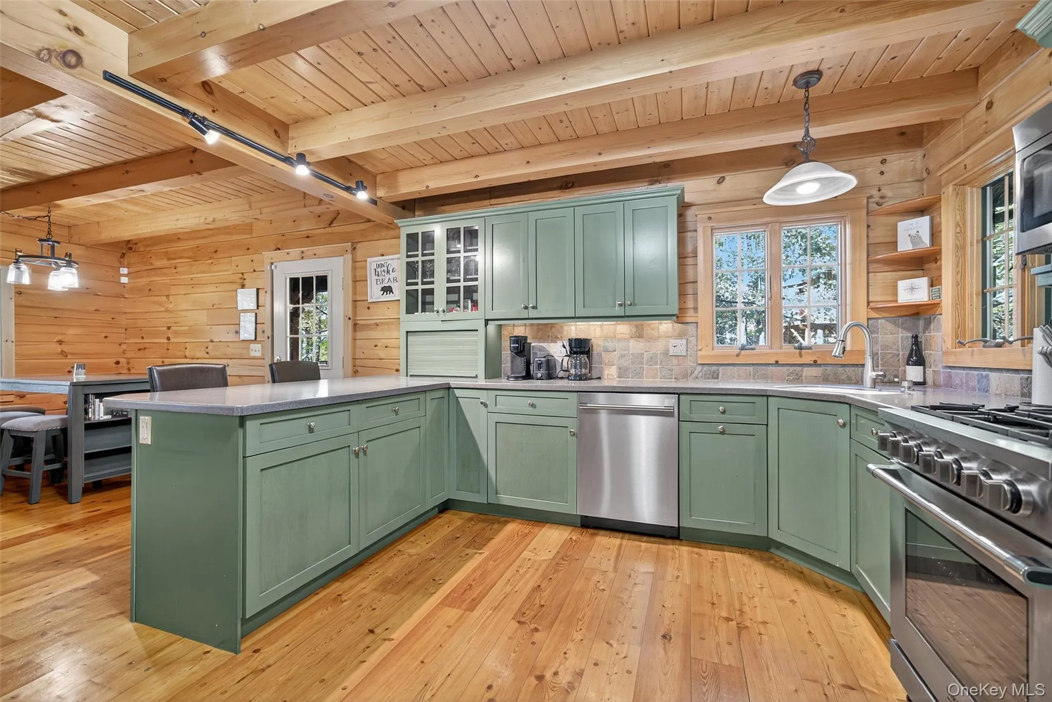 Kitchen with decorative light fixtures, green cabinetry, a peninsula, stainless steel appliances, and glass insert cabinets Kitchen with decorative light fixtures, green cabinetry, a peninsula, stainless steel appliances, and glass insert cabinets
