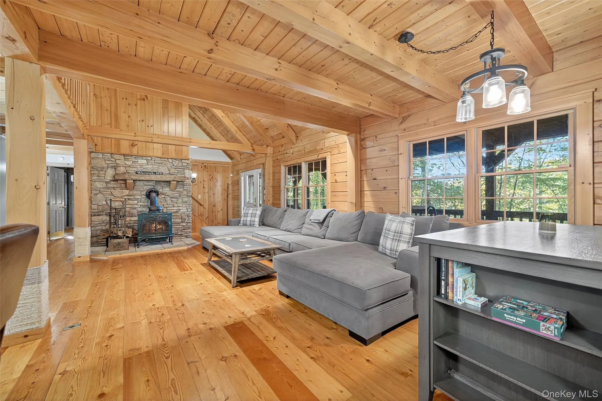 Living room featuring wood walls, a wood stove, light wood-style flooring, and wooden ceiling Living room featuring wood walls, a wood stove, light wood-style flooring, and wooden ceiling