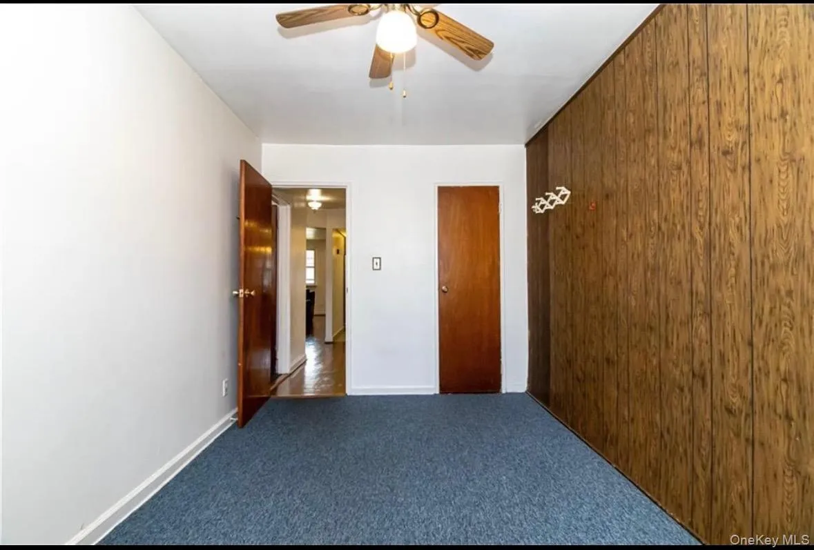 Carpeted empty room featuring wood walls and a ceiling fan Carpeted empty room featuring wood walls and a ceiling fan