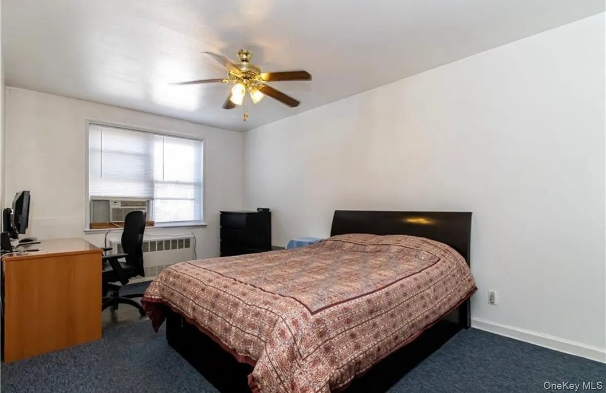 Bedroom featuring radiator, a ceiling fan, dark carpet, cooling unit, and a desk Bedroom featuring radiator, a ceiling fan, dark carpet, cooling unit, and a desk