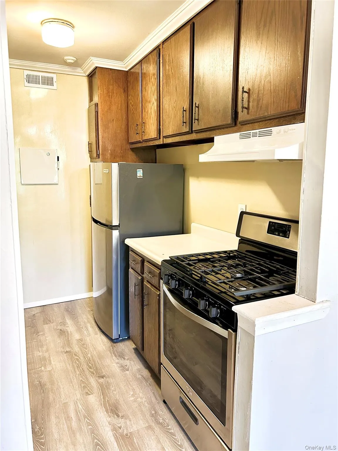 Kitchen with stainless steel appliances, light countertops, light wood finished floors, under cabinet range hood, and ornamental molding Kitchen with stainless steel appliances, light countertops, light wood finished floors, under cabinet range hood, and ornamental molding