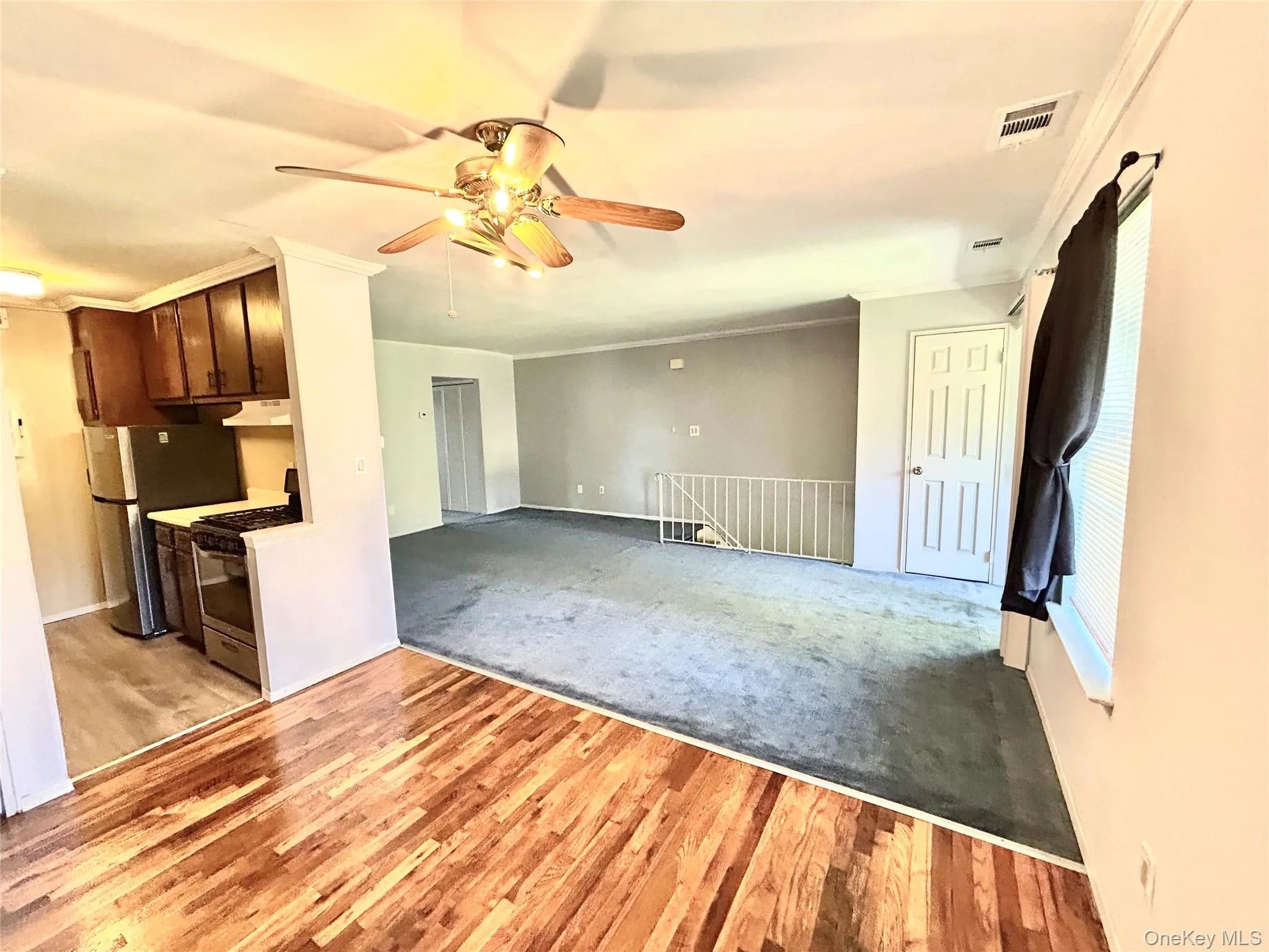 Unfurnished living room featuring ornamental molding, light wood finished floors, a ceiling fan, and light colored carpet Unfurnished living room featuring ornamental molding, light wood finished floors, a ceiling fan, and light colored carpet