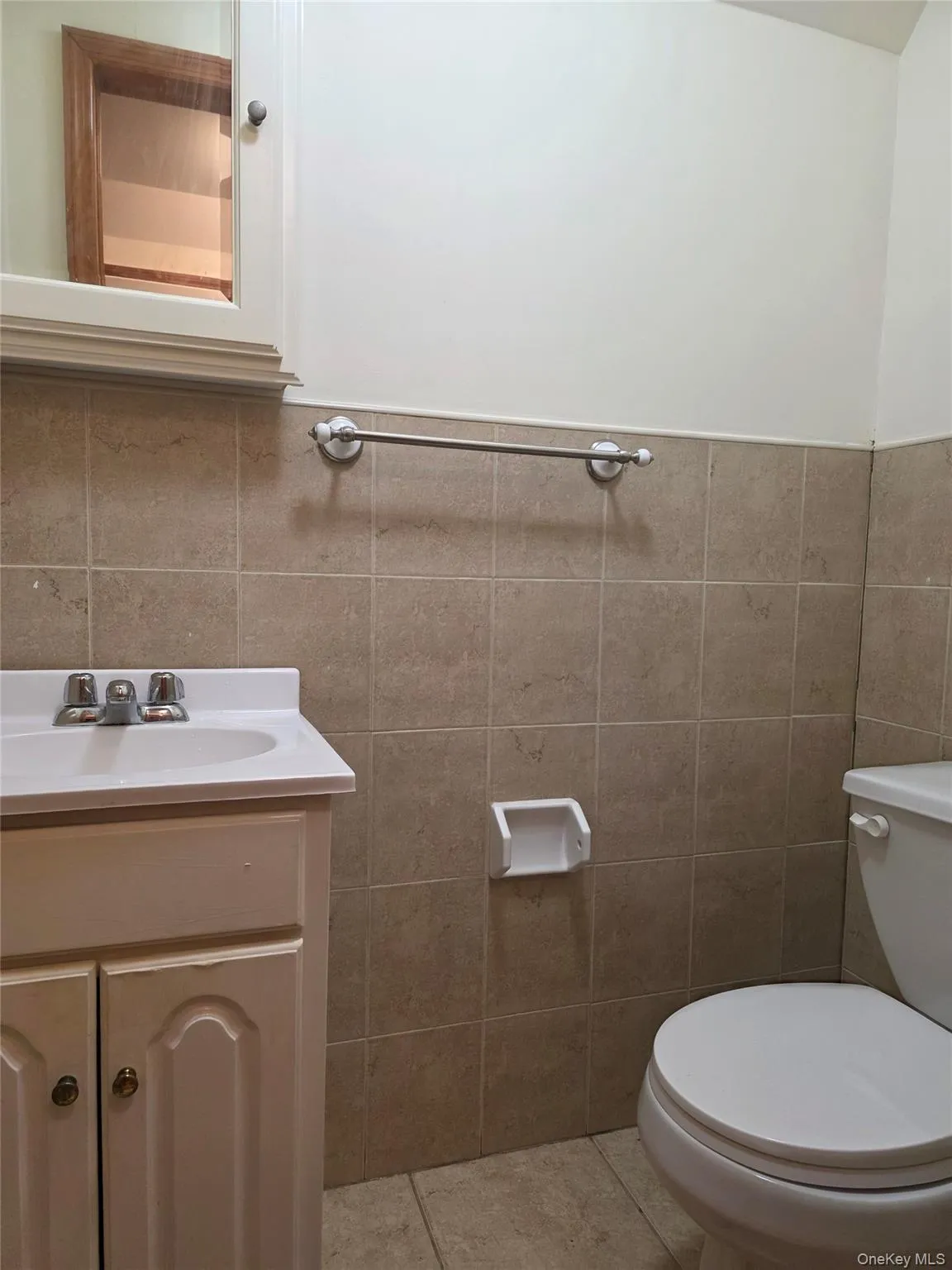 Half bath with tile walls, light tile patterned floors, vanity, and a wainscoted wall Half bath with tile walls, light tile patterned floors, vanity, and a wainscoted wall