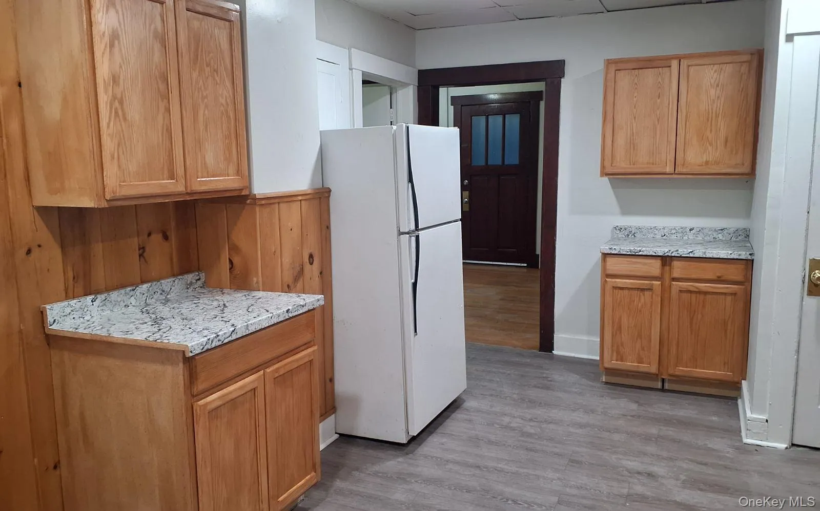 Kitchen with freestanding refrigerator, dark wood-type flooring, brown cabinets, and light stone countertops Kitchen with freestanding refrigerator, dark wood-type flooring, brown cabinets, and light stone countertops