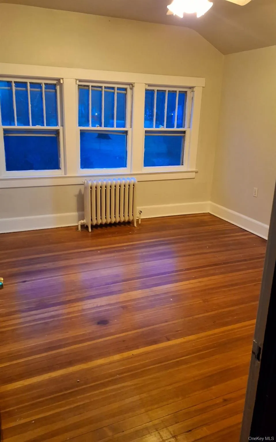Unfurnished room with radiator heating unit, vaulted ceiling, and dark wood-type flooring Unfurnished room with radiator heating unit, vaulted ceiling, and dark wood-type flooring