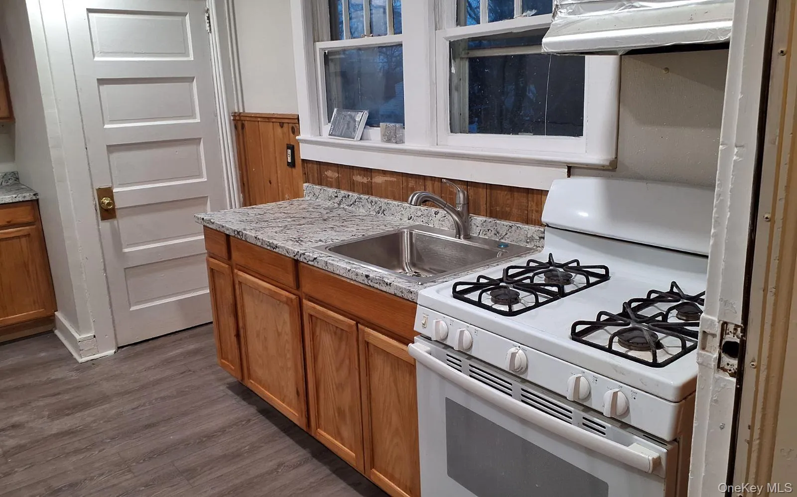 Kitchen featuring white gas stove, light countertops, ventilation hood, and brown cabinets Kitchen featuring white gas stove, light countertops, ventilation hood, and brown cabinets