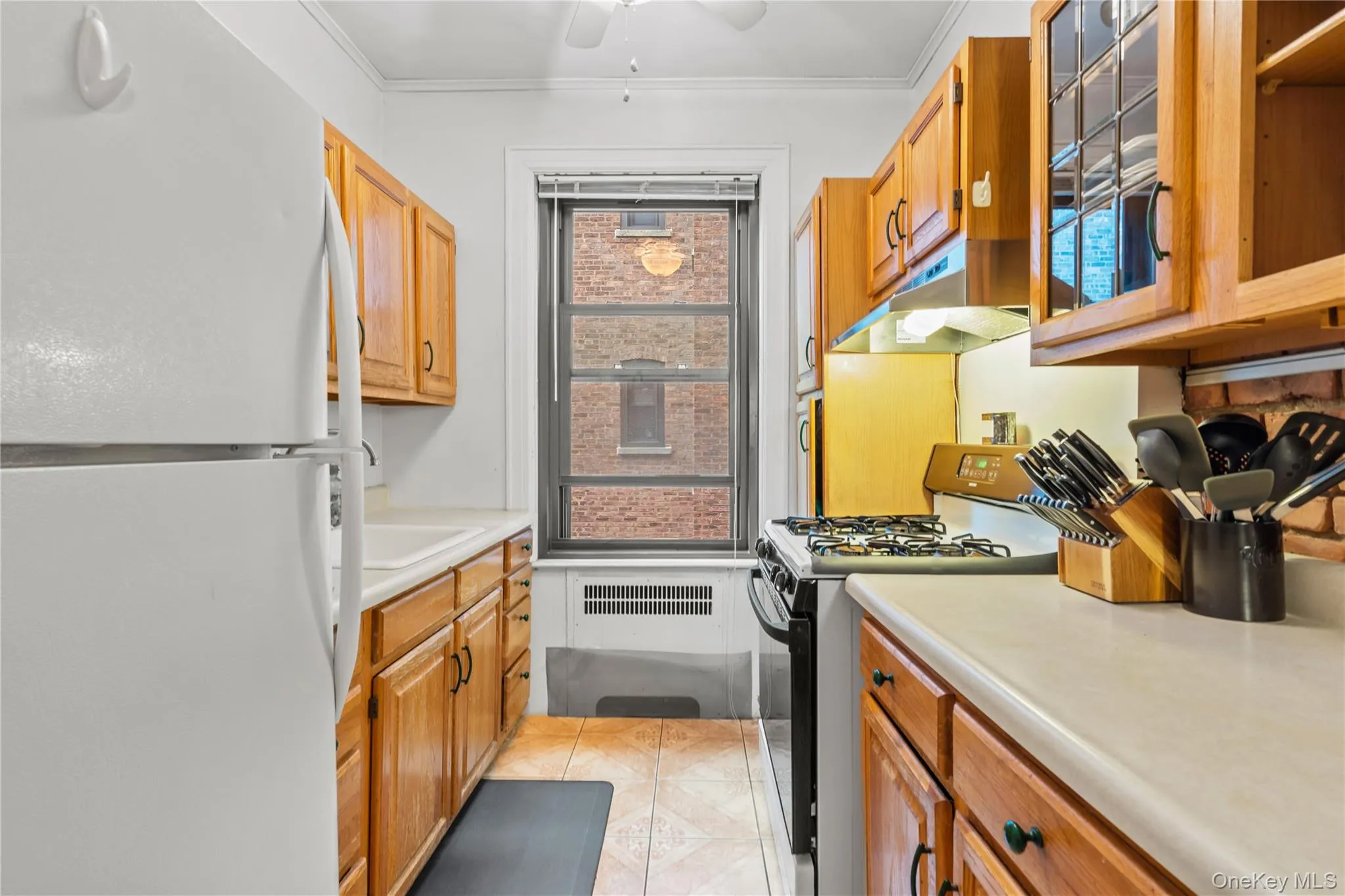 Kitchen featuring freestanding refrigerator, black gas range, healthy amount of natural light, under cabinet range hood, and ornamental molding Kitchen featuring freestanding refrigerator, black gas range, healthy amount of natural light, under cabinet range hood, and ornamental molding