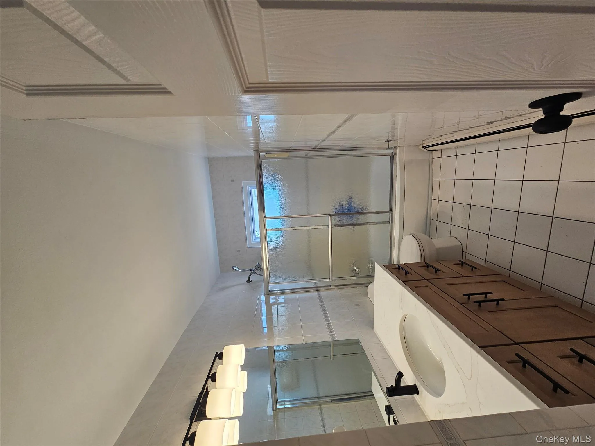 Bathroom with combined bath / shower with glass door, vanity, light tile patterned flooring, and tile walls Bathroom with combined bath / shower with glass door, vanity, light tile patterned flooring, and tile walls