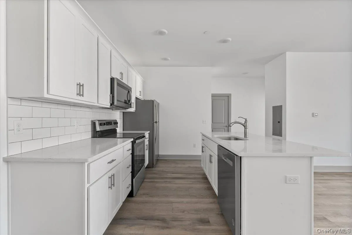 Kitchen featuring appliances with stainless steel finishes, a center island with sink, white cabinetry, light stone counters, and light wood-style floors Kitchen featuring appliances with stainless steel finishes, a center island with sink, white cabinetry, light stone counters, and light wood-style floors