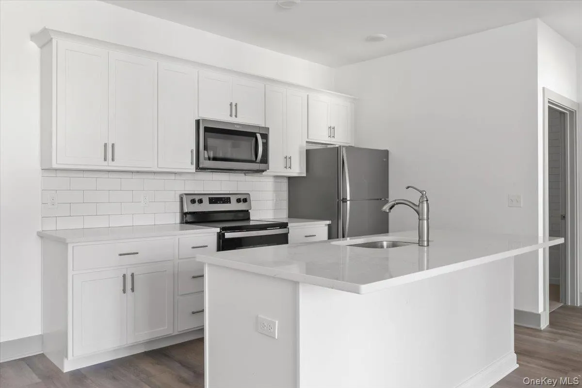 Kitchen featuring appliances with stainless steel finishes, light stone counters, white cabinets, backsplash, and dark wood finished floors Kitchen featuring appliances with stainless steel finishes, light stone counters, white cabinets, backsplash, and dark wood finished floors