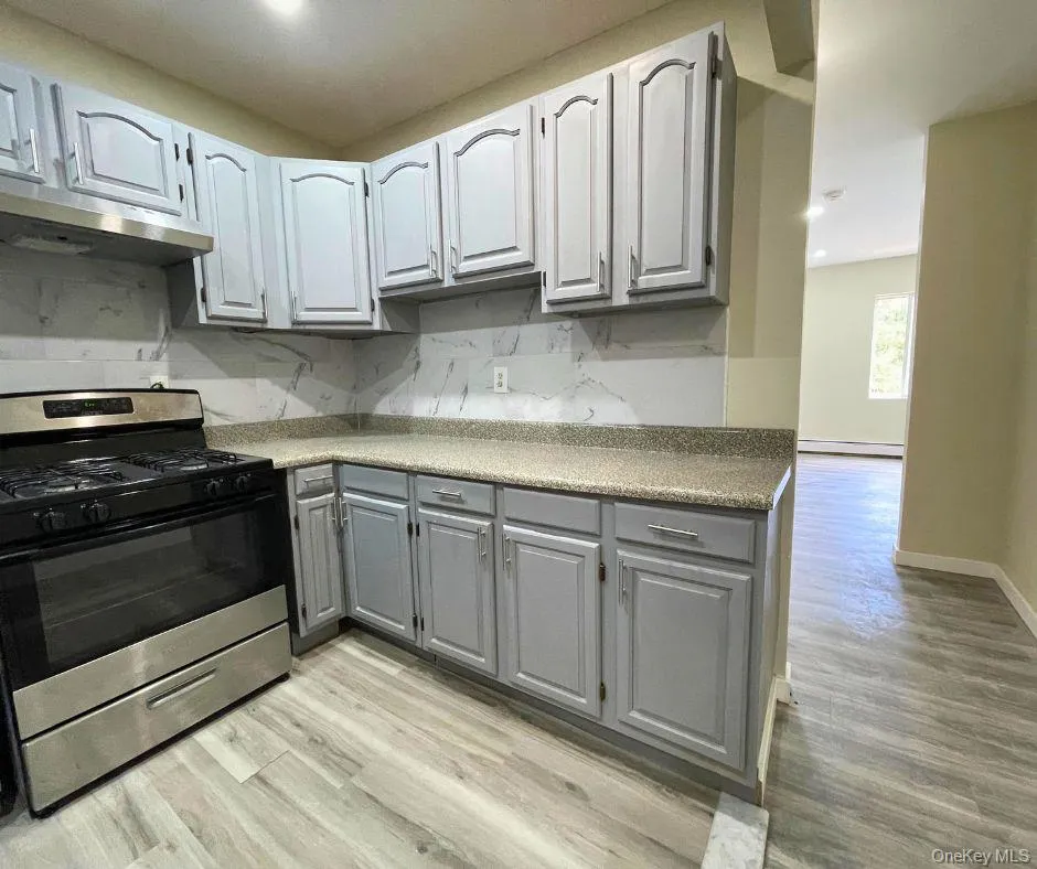 Kitchen with gas range, gray cabinets, backsplash, light wood finished floors, and recessed lighting Kitchen with gas range, gray cabinets, backsplash, light wood finished floors, and recessed lighting