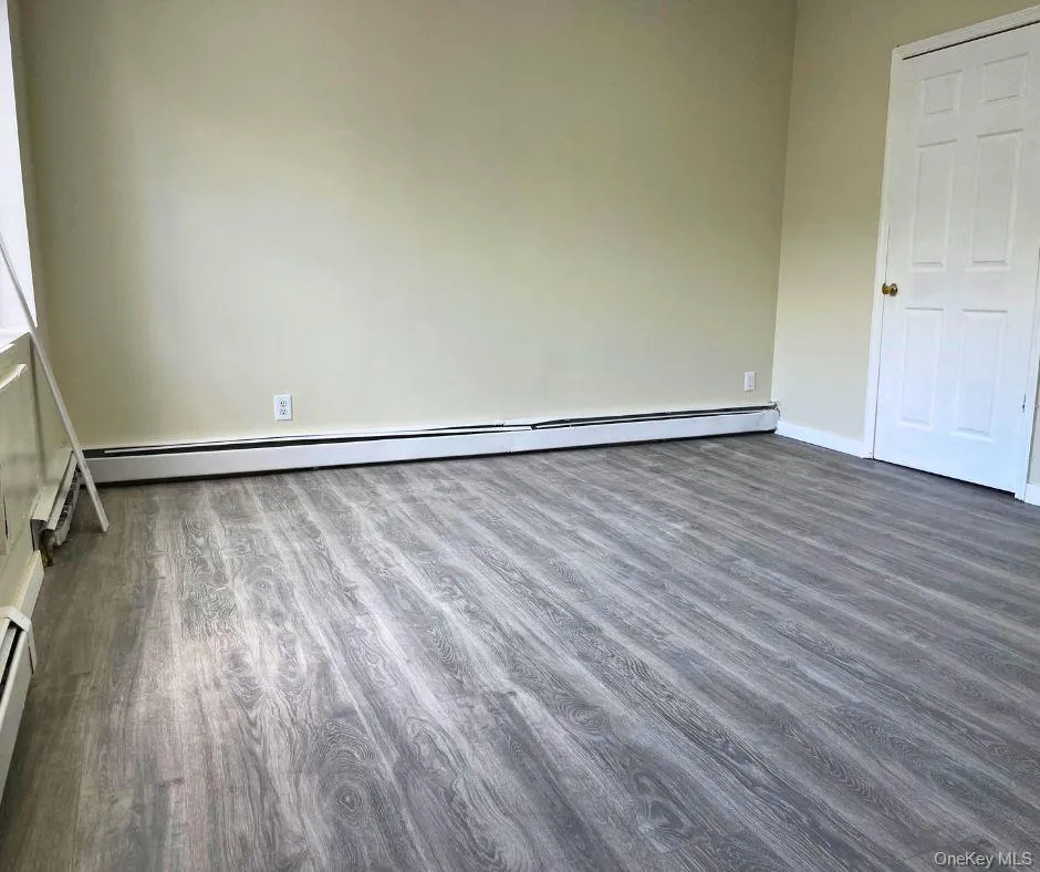 Empty room featuring dark wood finished floors and baseboard heating Empty room featuring dark wood finished floors and baseboard heating