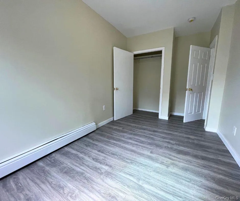 Unfurnished bedroom with baseboard heating, wood finished floors, and a closet Unfurnished bedroom with baseboard heating, wood finished floors, and a closet