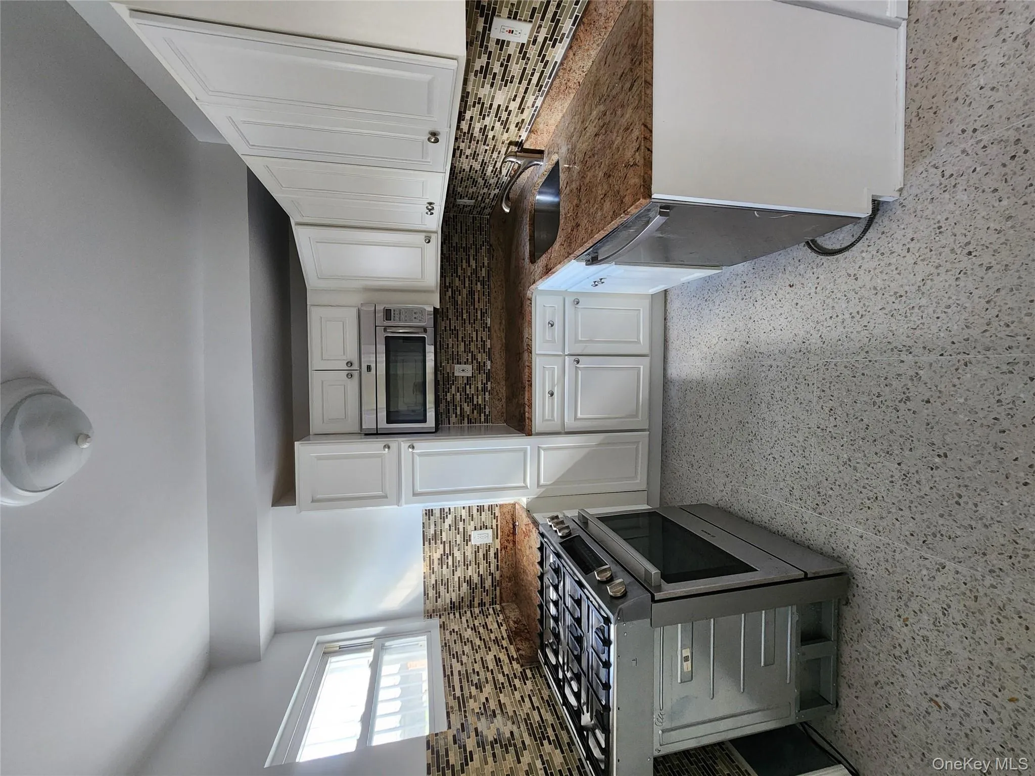Kitchen with range, decorative backsplash, white cabinetry, dishwasher, and dark stone counters Kitchen with range, decorative backsplash, white cabinetry, dishwasher, and dark stone counters