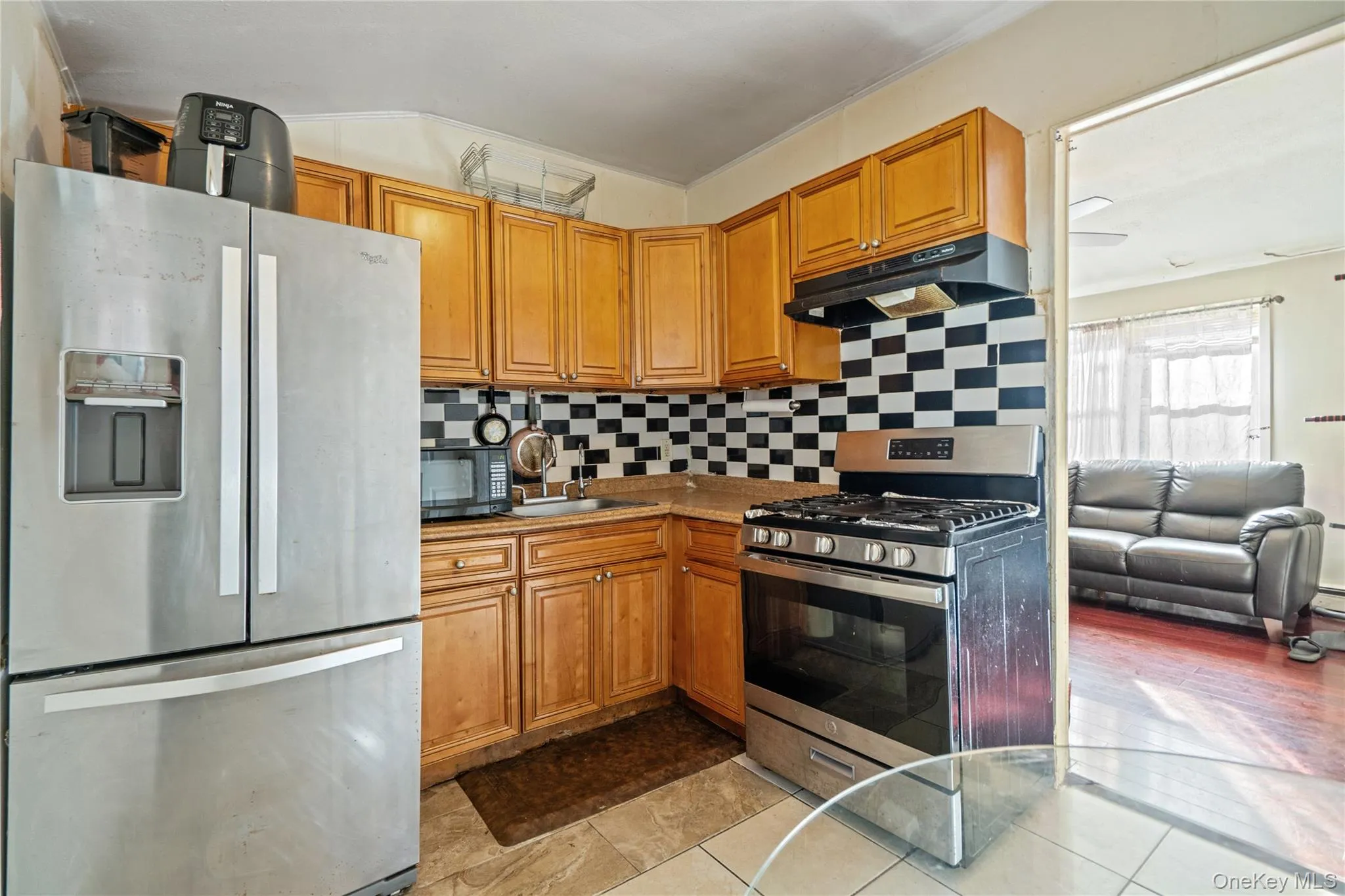 Kitchen with appliances with stainless steel finishes, tasteful backsplash, brown cabinets, under cabinet range hood, and light tile patterned floors Kitchen with appliances with stainless steel finishes, tasteful backsplash, brown cabinets, under cabinet range hood, and light tile patterned floors