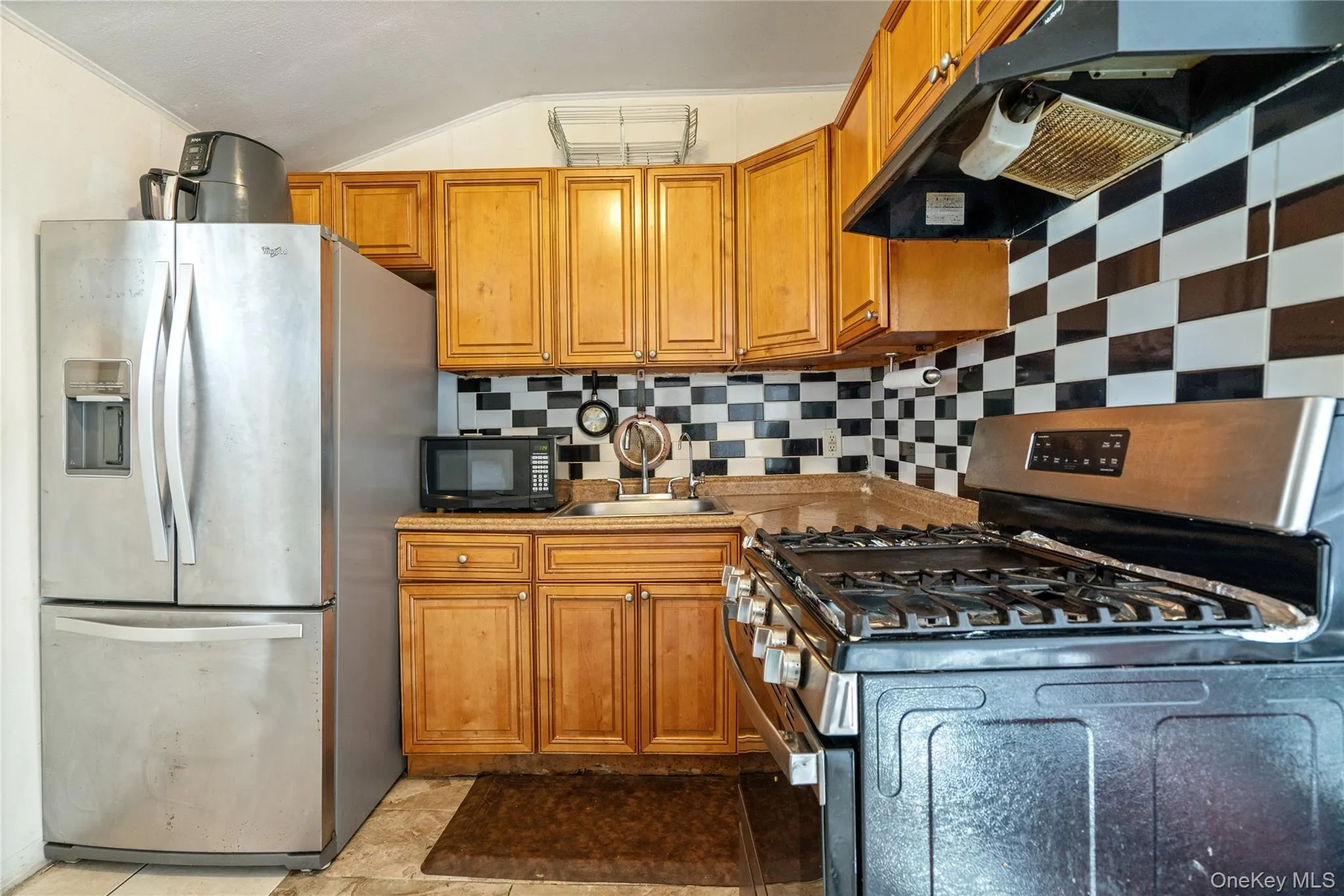 Kitchen with stainless steel appliances, decorative backsplash, ventilation hood, brown cabinets, and lofted ceiling Kitchen with stainless steel appliances, decorative backsplash, ventilation hood, brown cabinets, and lofted ceiling