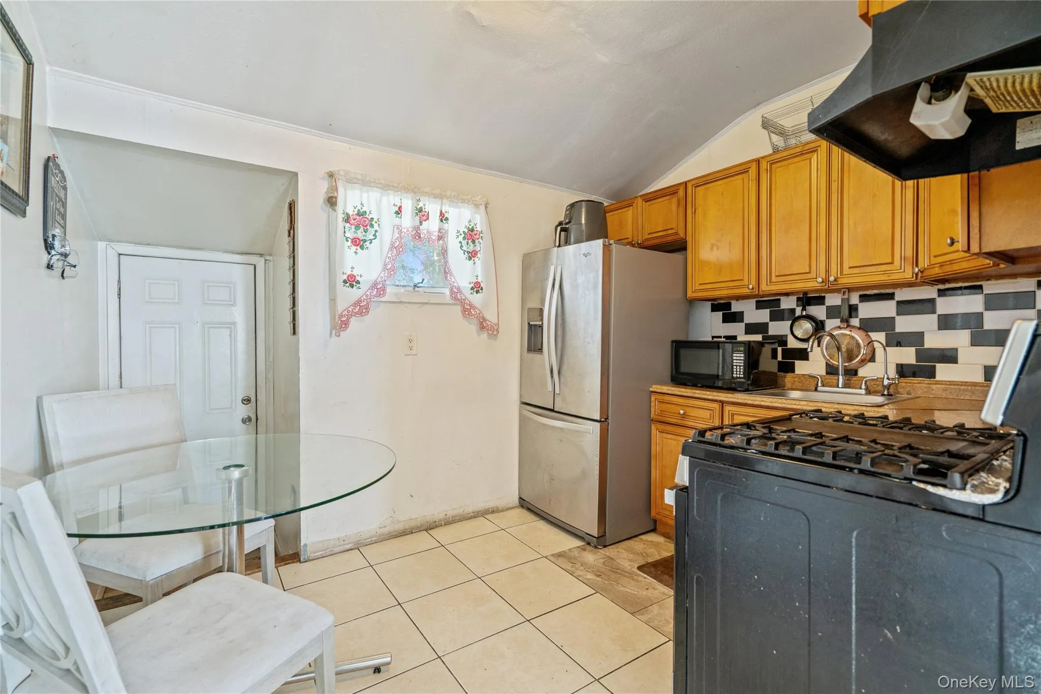 Kitchen with range with gas stovetop, brown cabinets, exhaust hood, vaulted ceiling, and light tile patterned floors Kitchen with range with gas stovetop, brown cabinets, exhaust hood, vaulted ceiling, and light tile patterned floors