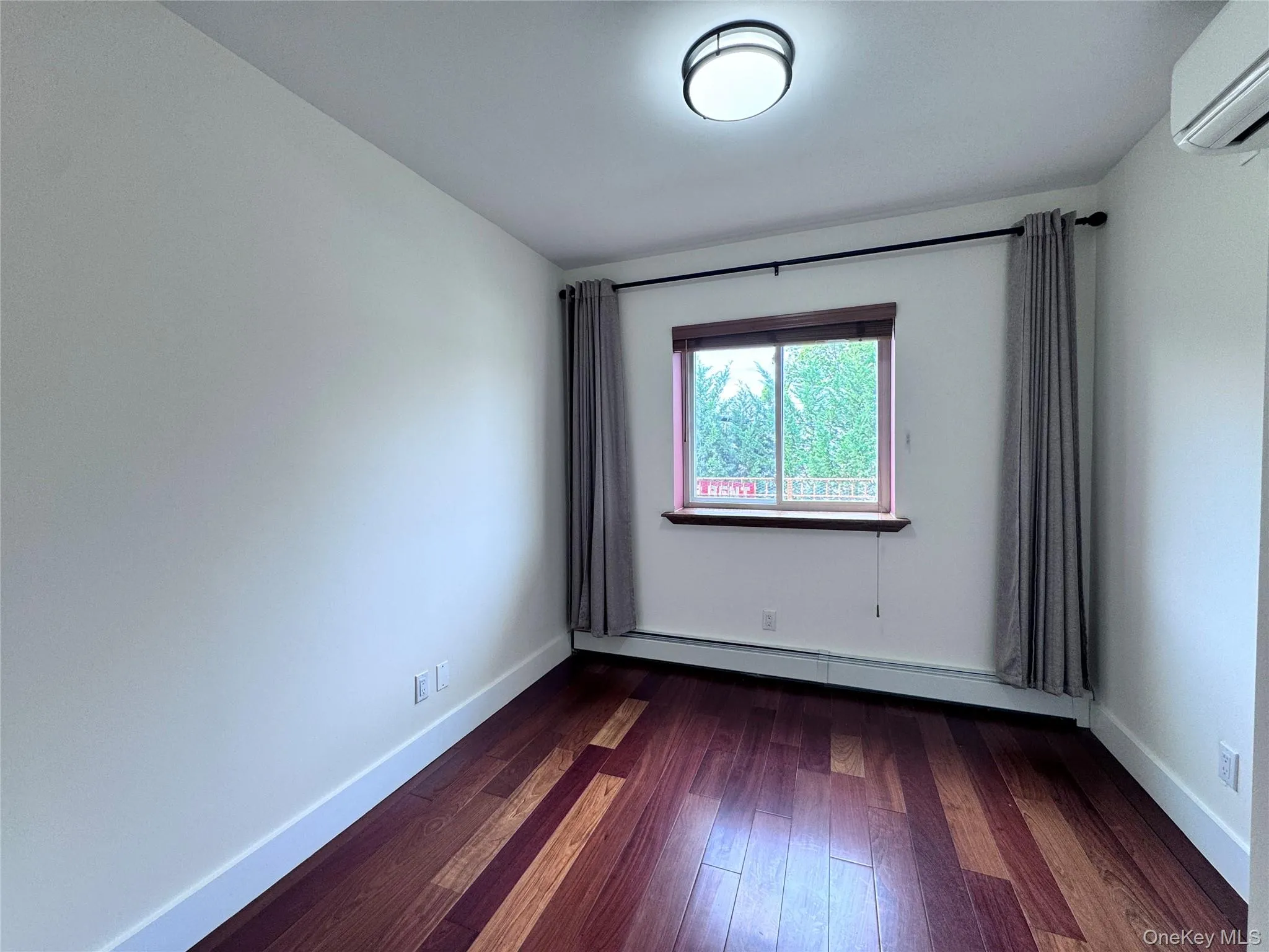 Unfurnished room with dark wood-type flooring, a wall mounted air conditioner, and a baseboard heating unit Unfurnished room with dark wood-type flooring, a wall mounted air conditioner, and a baseboard heating unit