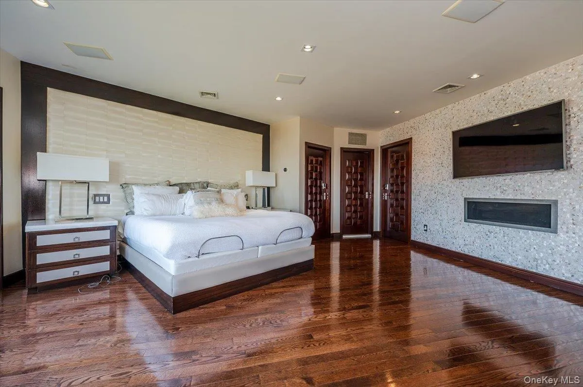 Bedroom with dark wood-type flooring, recessed lighting, wallpapered walls, and multiple closets Bedroom with dark wood-type flooring, recessed lighting, wallpapered walls, and multiple closets