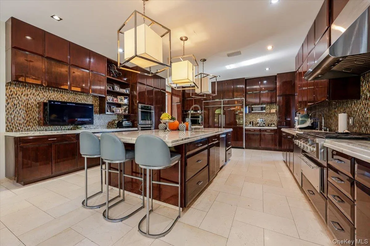 Kitchen featuring a breakfast bar, tasteful backsplash, a kitchen island with sink, open shelves, and under cabinet range hood Kitchen featuring a breakfast bar, tasteful backsplash, a kitchen island with sink, open shelves, and under cabinet range hood