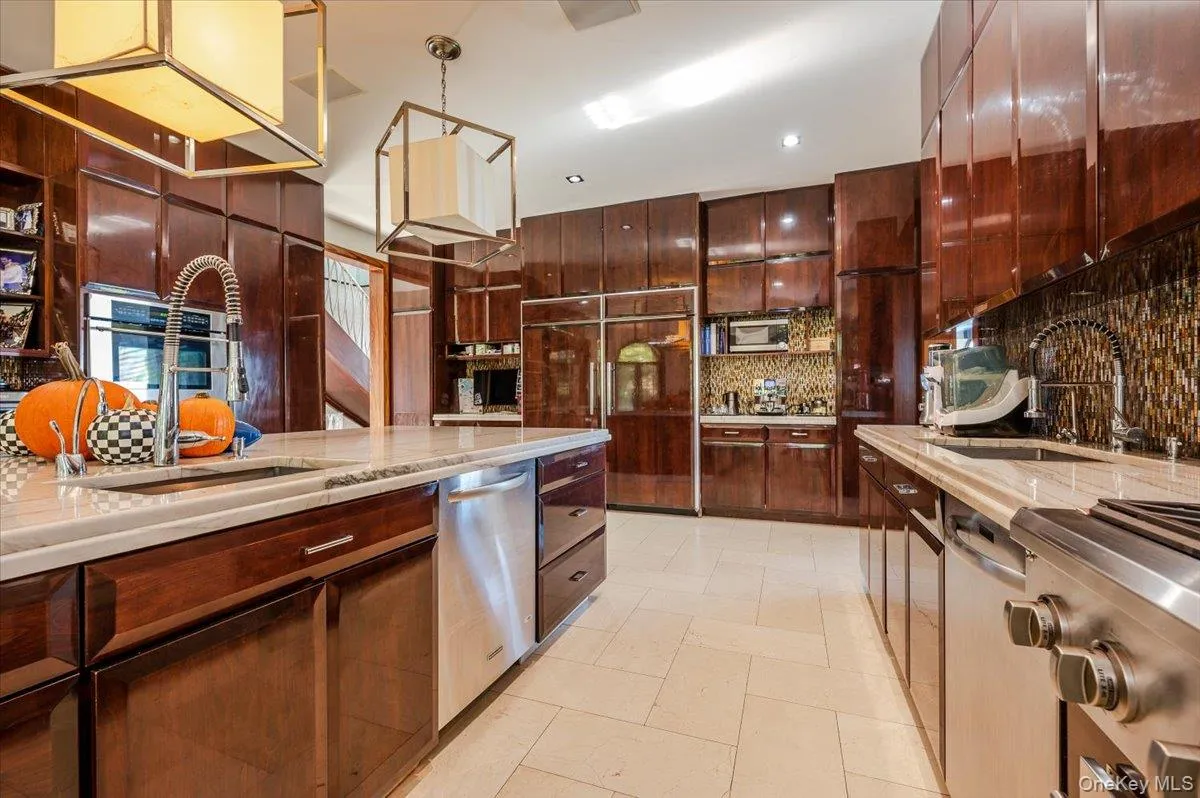 Kitchen with stainless steel appliances, backsplash, hanging light fixtures, and light stone countertops Kitchen with stainless steel appliances, backsplash, hanging light fixtures, and light stone countertops