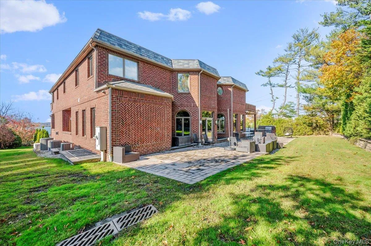 Rear view of property with brick siding, a patio area, a lawn, and a high end roof Rear view of property with brick siding, a patio area, a lawn, and a high end roof