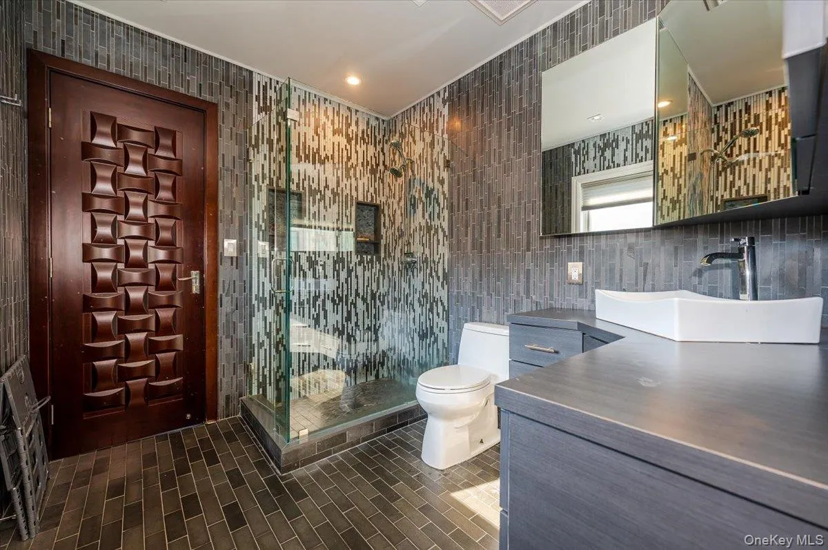Bathroom with tile walls, vanity, a shower stall, dark tile patterned flooring, and recessed lighting Bathroom with tile walls, vanity, a shower stall, dark tile patterned flooring, and recessed lighting