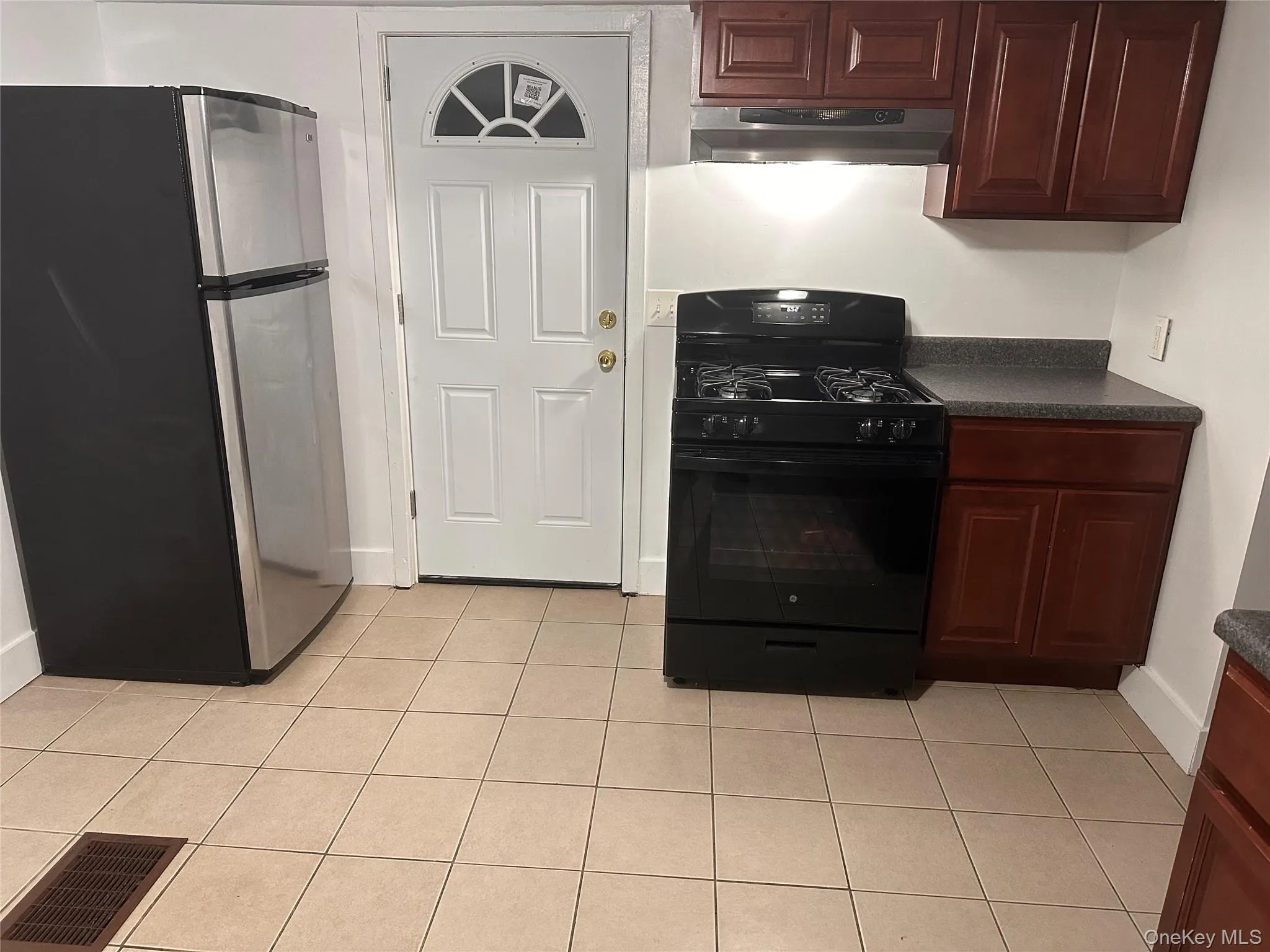 Kitchen featuring black range with gas stovetop, freestanding refrigerator, dark countertops, light tile patterned flooring, and range hood Kitchen featuring black range with gas stovetop, freestanding refrigerator, dark countertops, light tile patterned flooring, and range hood