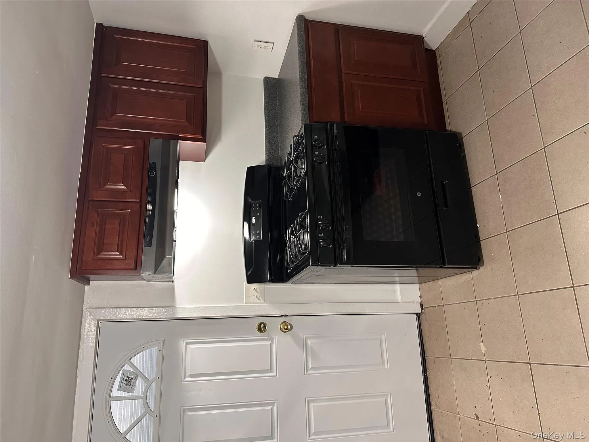 Kitchen featuring black gas stove, dark countertops, range hood, and light tile patterned flooring Kitchen featuring black gas stove, dark countertops, range hood, and light tile patterned flooring