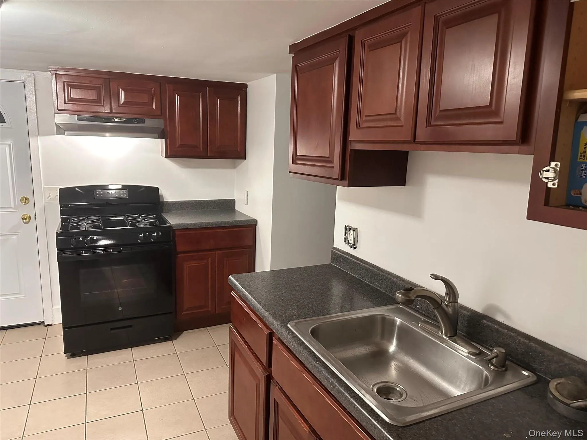 Kitchen with black gas stove, dark countertops, light tile patterned floors, and under cabinet range hood Kitchen with black gas stove, dark countertops, light tile patterned floors, and under cabinet range hood