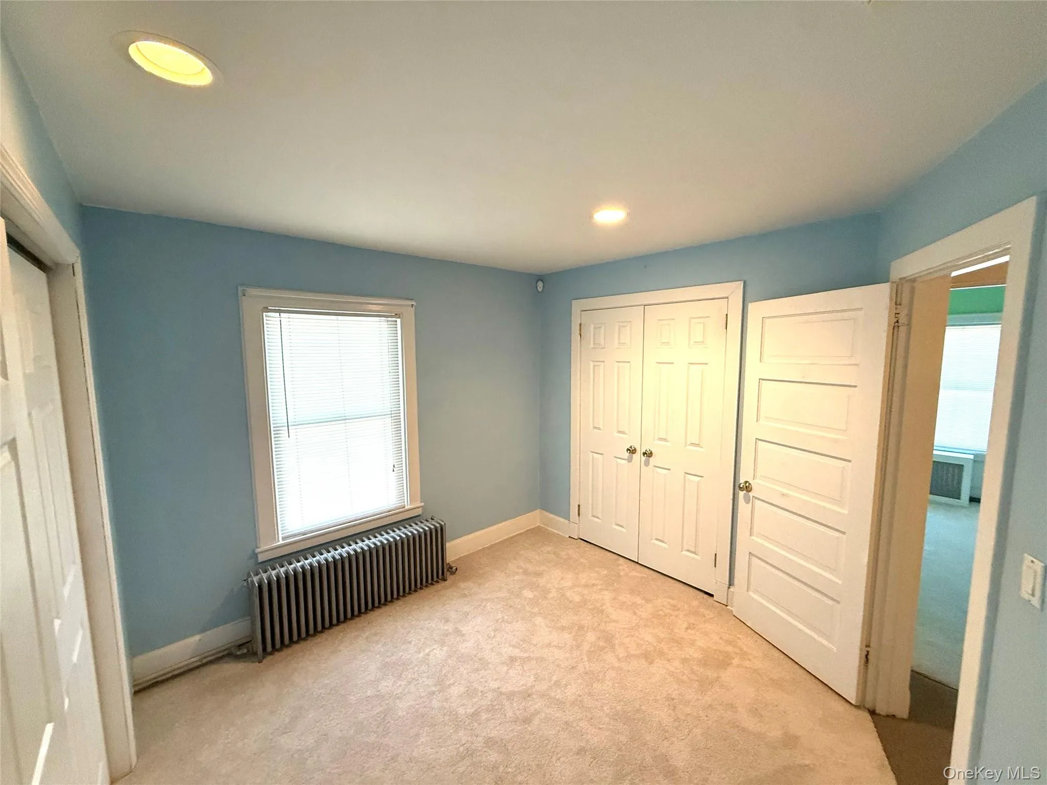 Unfurnished bedroom with a closet, radiator heating unit, carpet floors, and recessed lighting Unfurnished bedroom with a closet, radiator heating unit, carpet floors, and recessed lighting